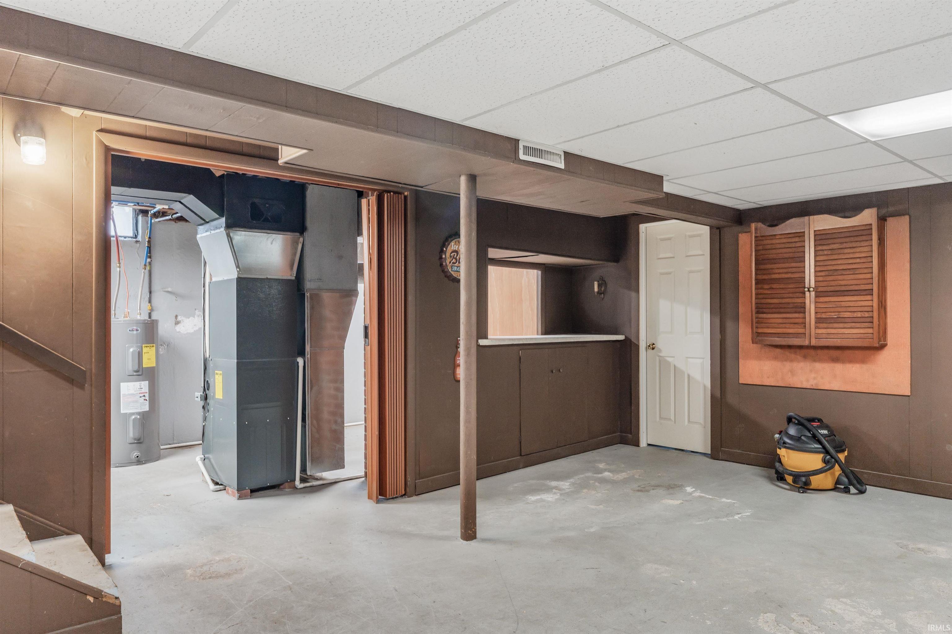 Finished basement featuring a drop ceiling, electric water heater, and heating unit