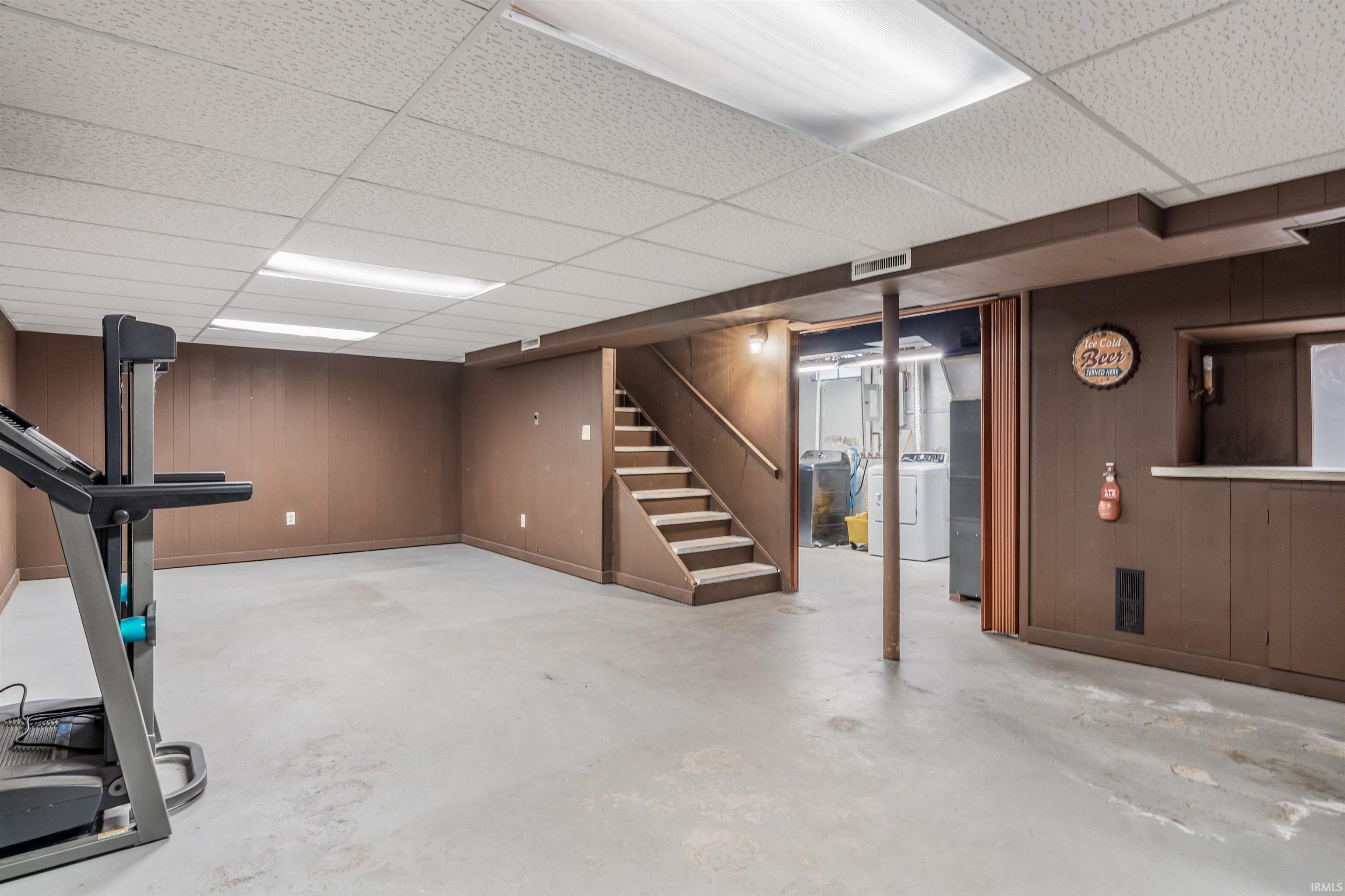 Workout area with wood walls, concrete flooring, washer / clothes dryer, and a paneled ceiling