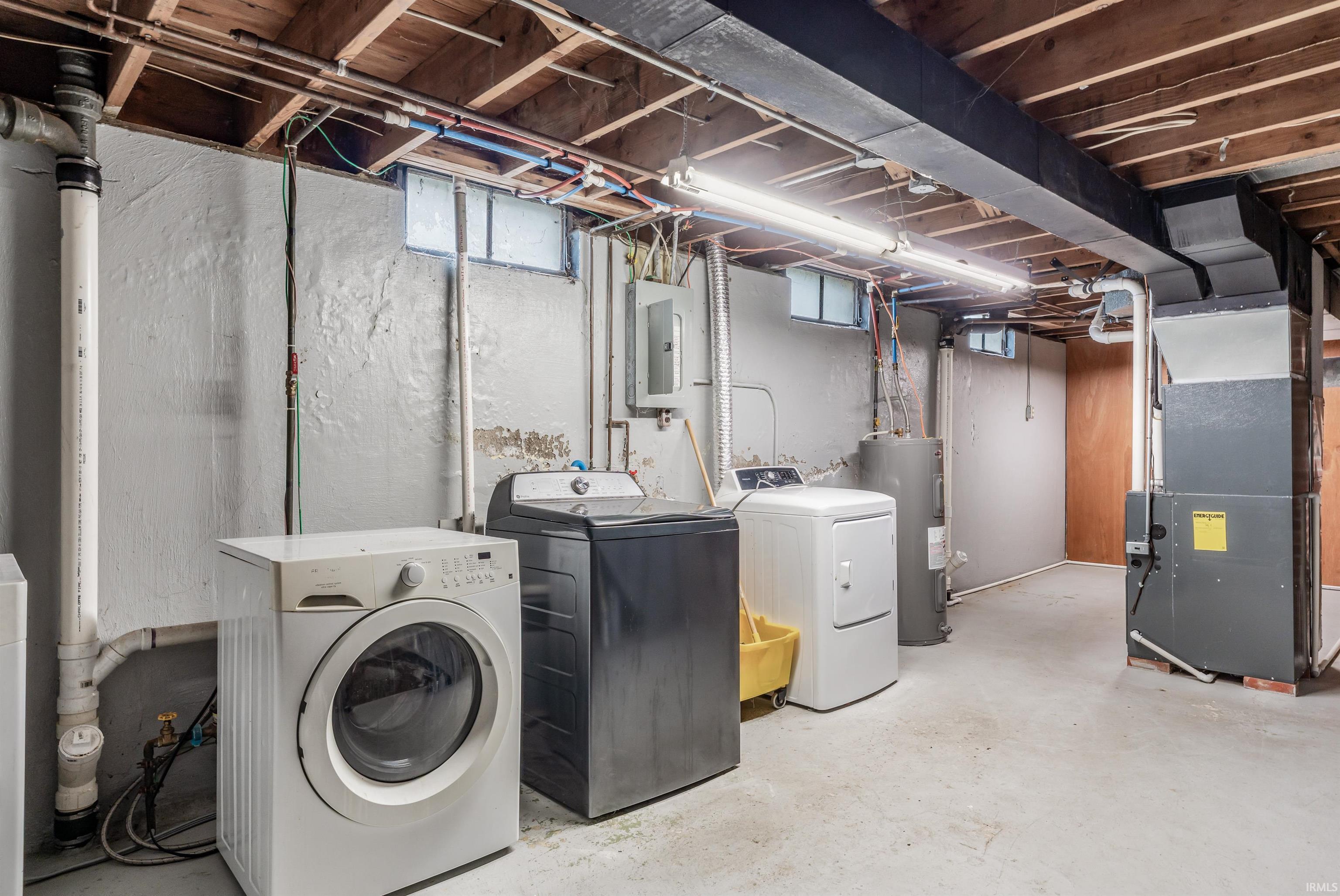 Washroom with unfinished concrete flooring, separate washer and dryer, heating unit, water heater, and healthy amount of natural light
