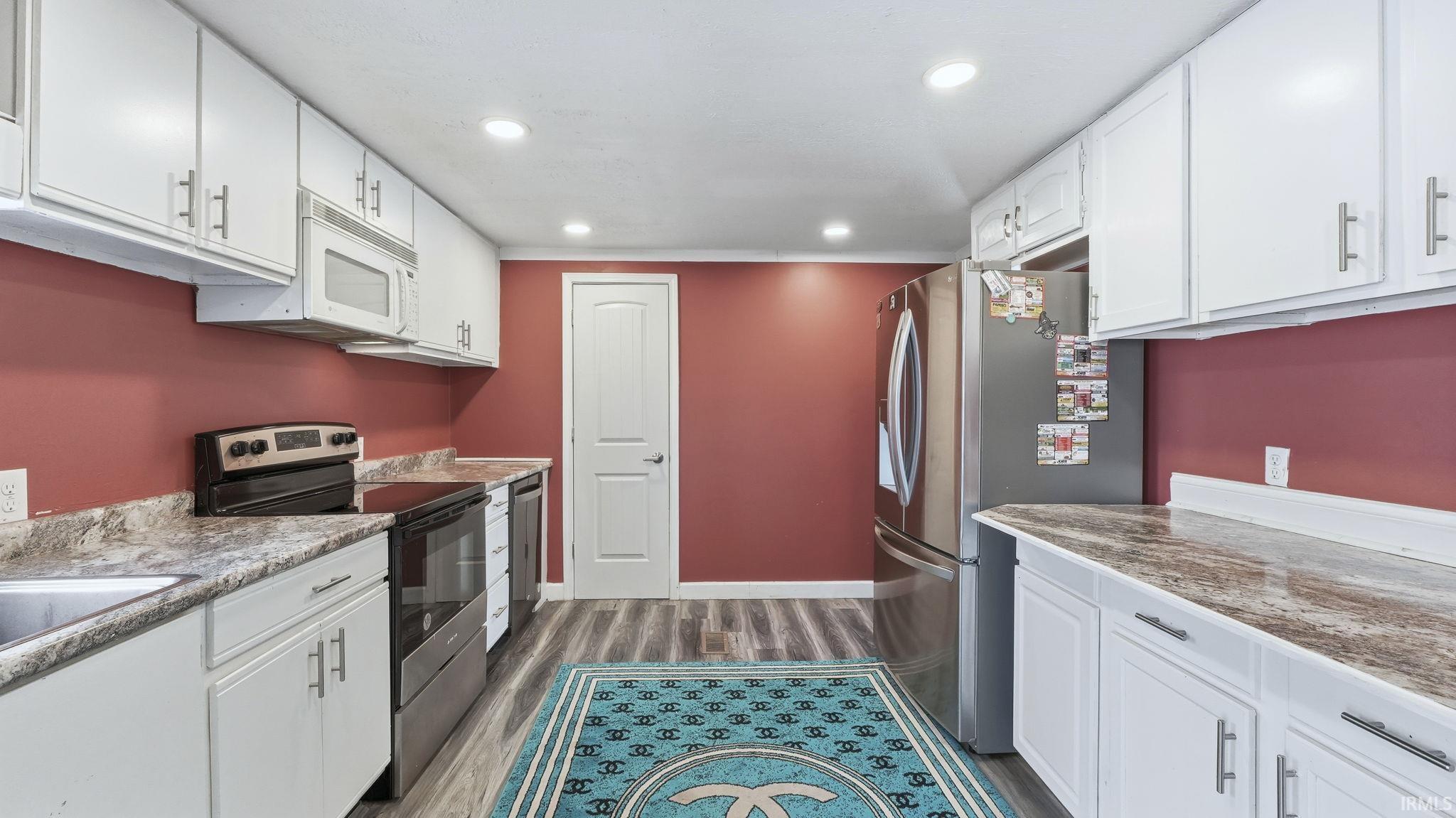 Kitchen featuring white cabinets, appliances with stainless steel finishes, dark wood-style flooring, recessed lighting, and light stone countertops