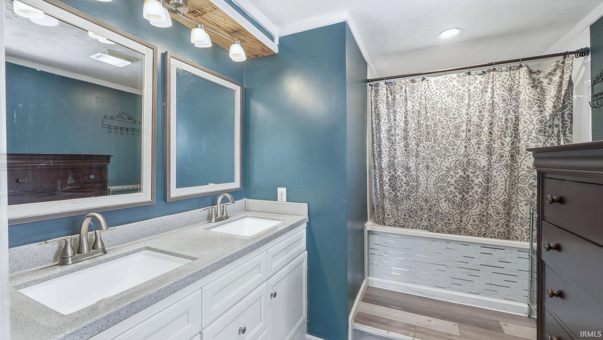 Bathroom with double vanity, crown molding, light wood-style floors, and curtained shower