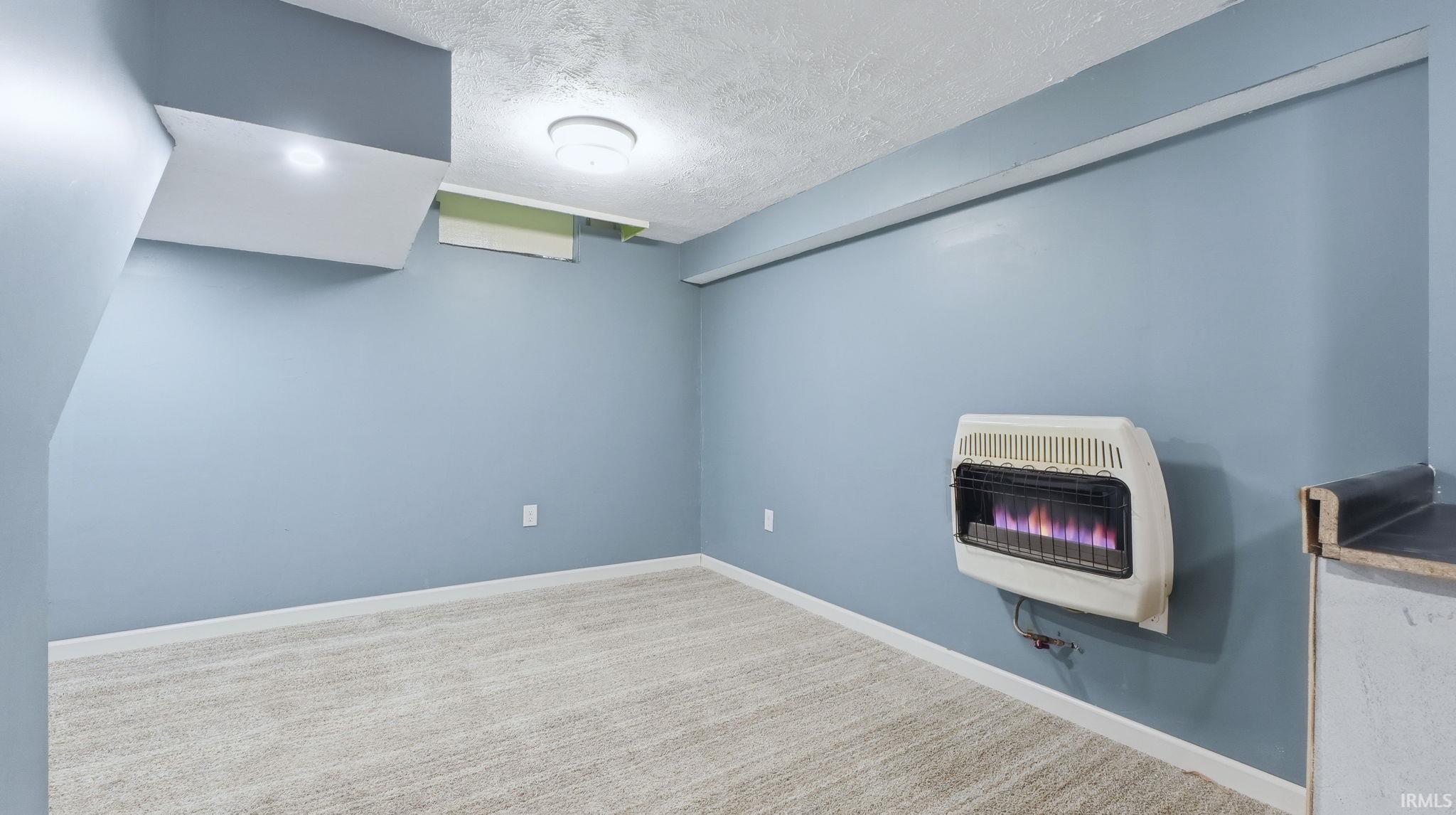 Finished below grade area featuring a textured ceiling, heating unit, and carpet floors