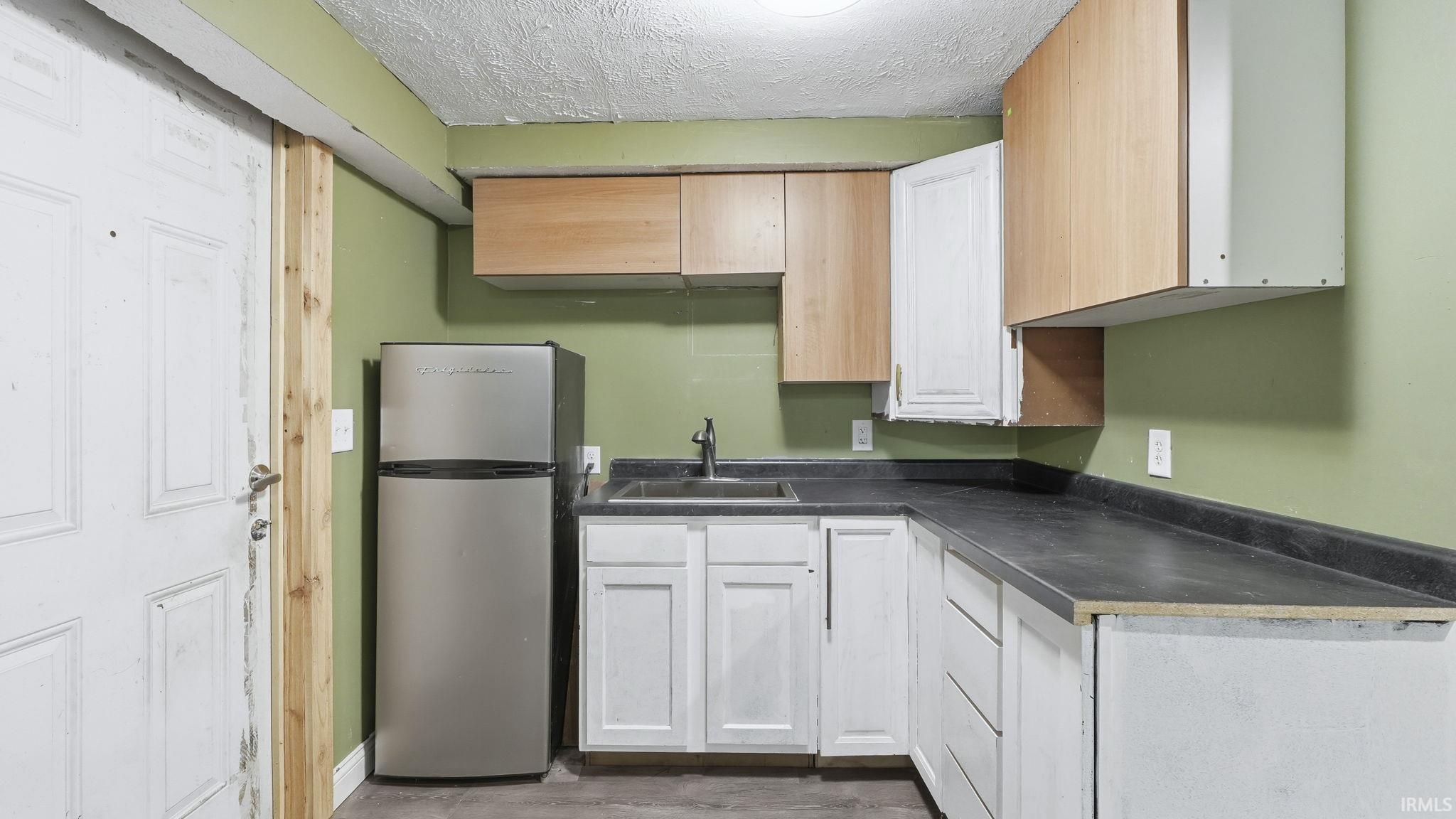 Kitchen featuring freestanding refrigerator, a textured ceiling, dark countertops, and white cabinetry