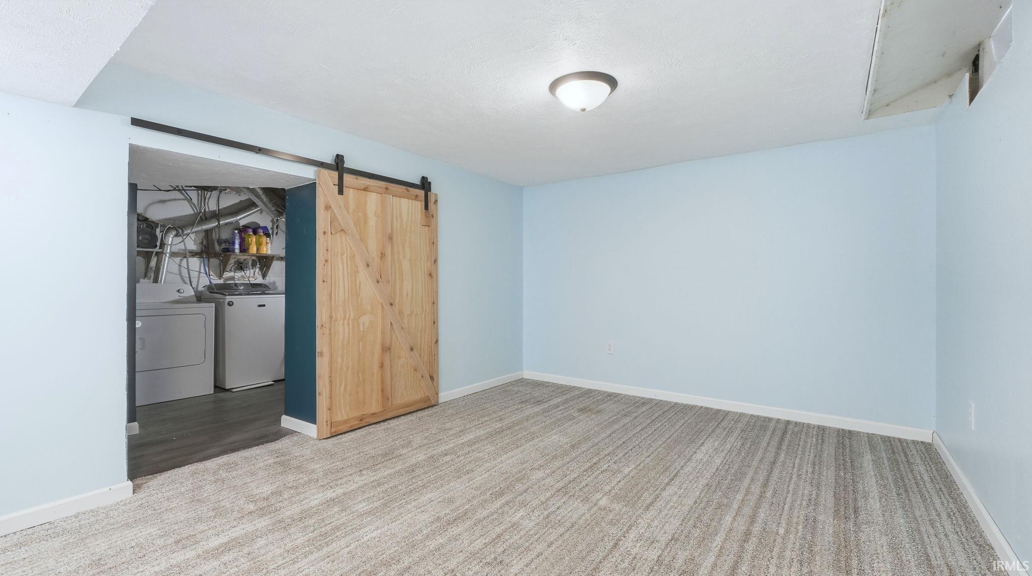 Unfurnished room with carpet floors, independent washer and dryer, and a barn door