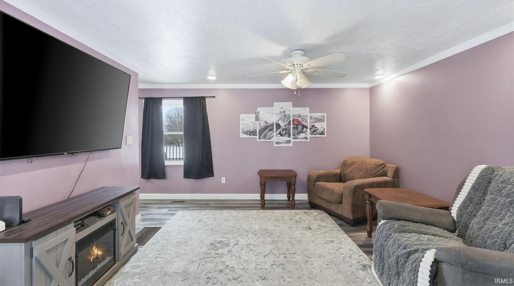 Living area with a ceiling fan, dark wood finished floors, crown molding, and a glass covered fireplace