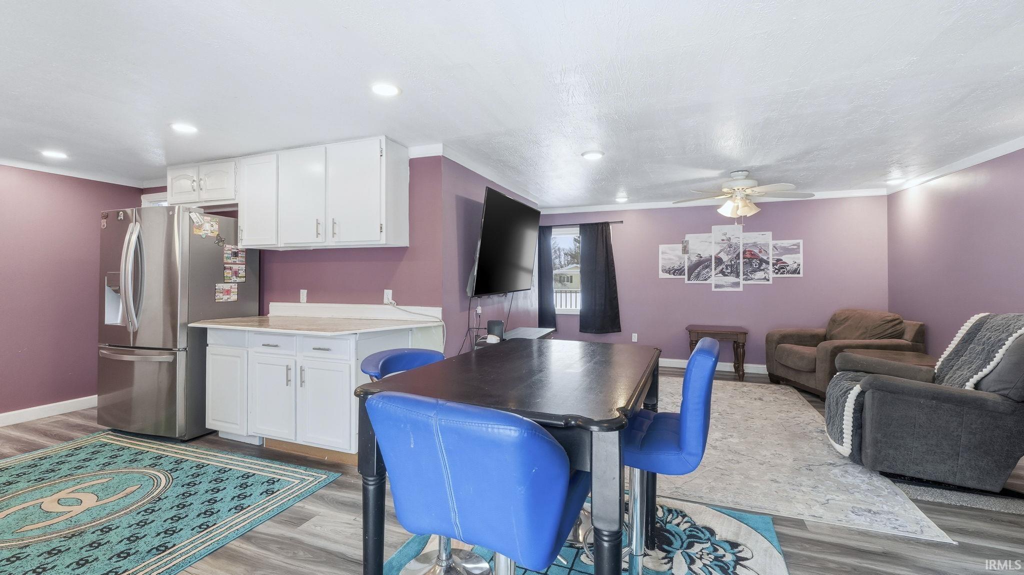 Kitchen featuring light countertops, white cabinets, stainless steel refrigerator with ice dispenser, light wood finished floors, and ornamental molding
