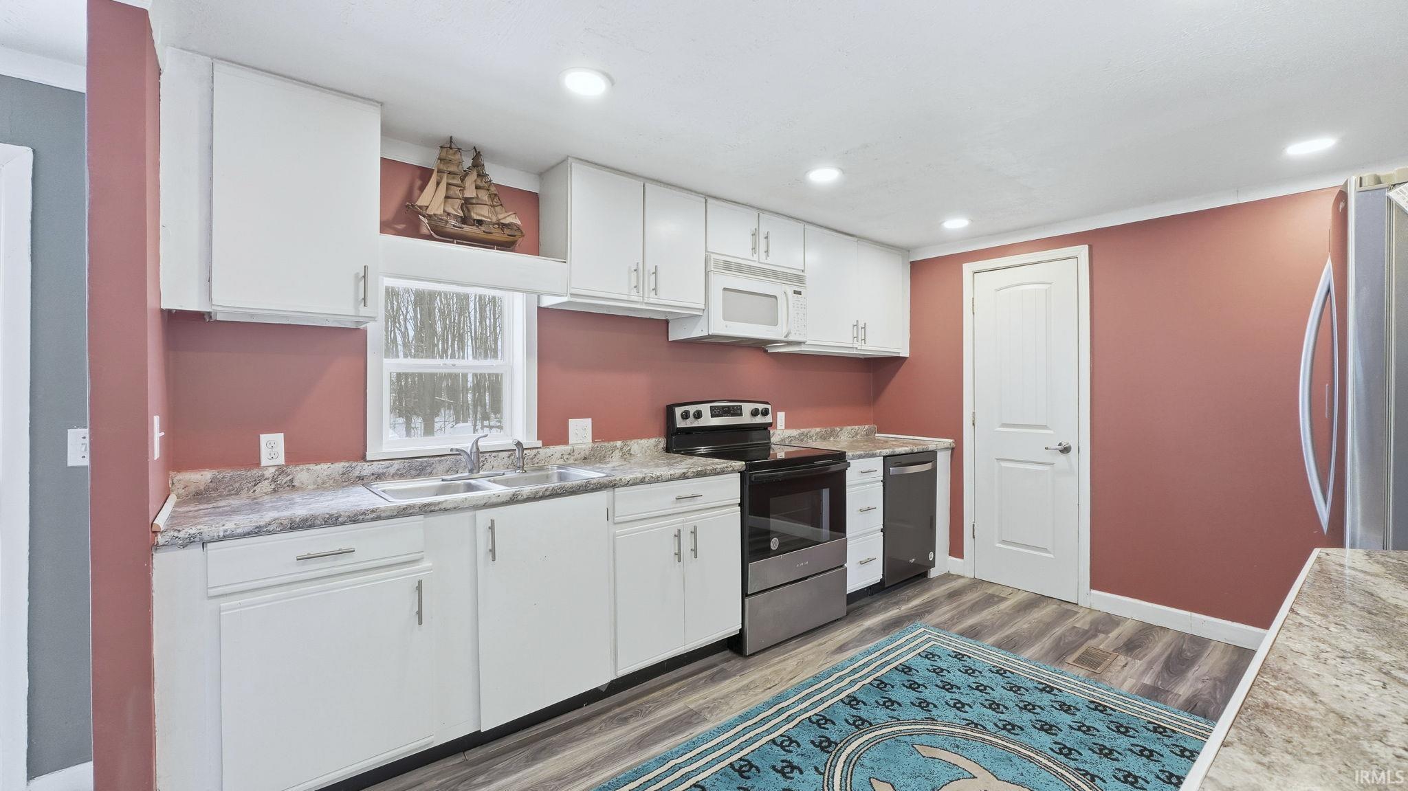 Kitchen featuring white cabinetry, stainless steel appliances, light countertops, dark wood-style floors, and recessed lighting