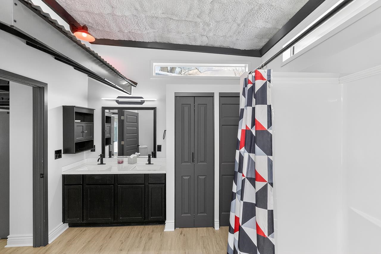 Bathroom with double vanity, light wood-style flooring, a shower with shower curtain, and a closet