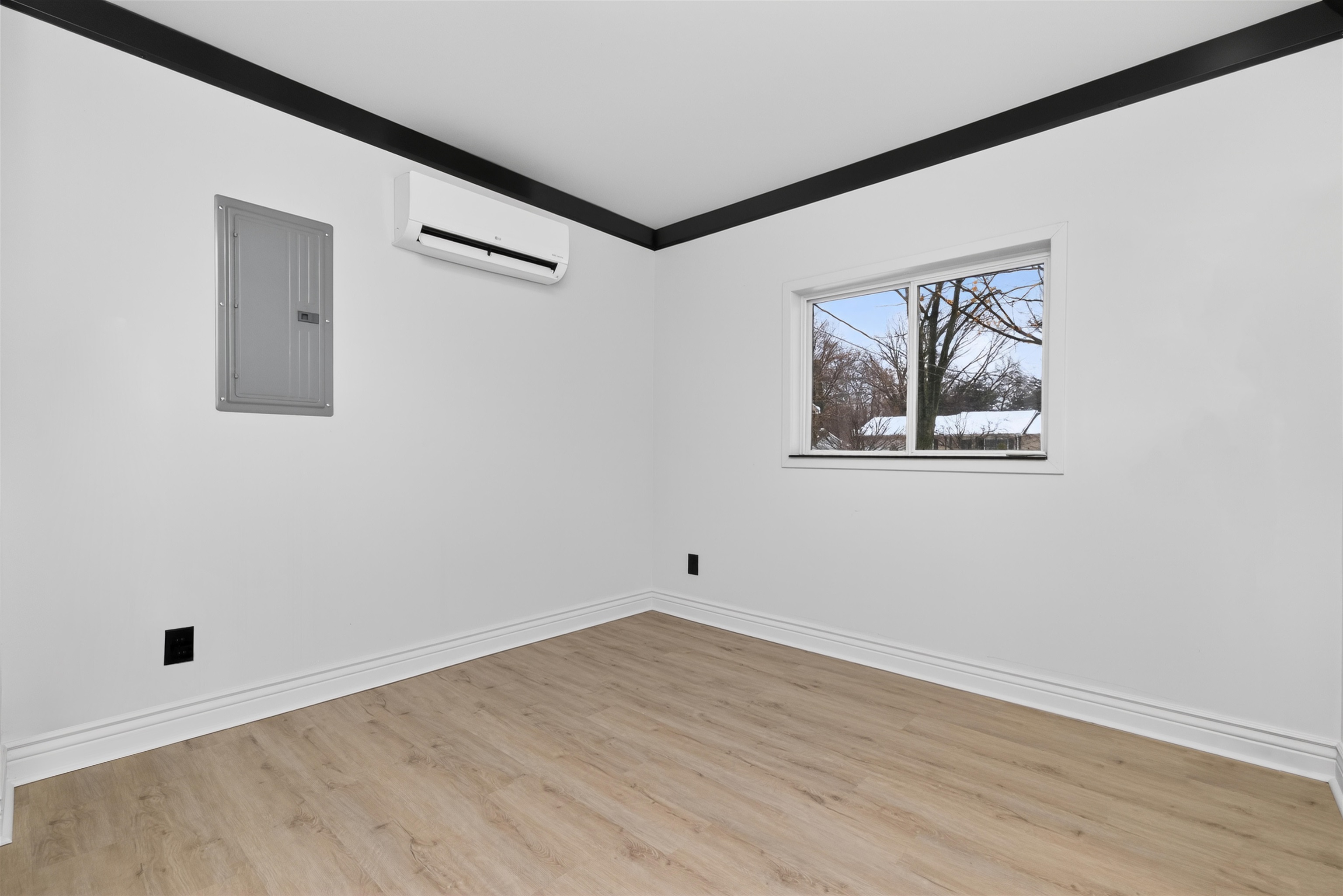 Spare room featuring electric panel, light wood-type flooring, and an AC wall unit