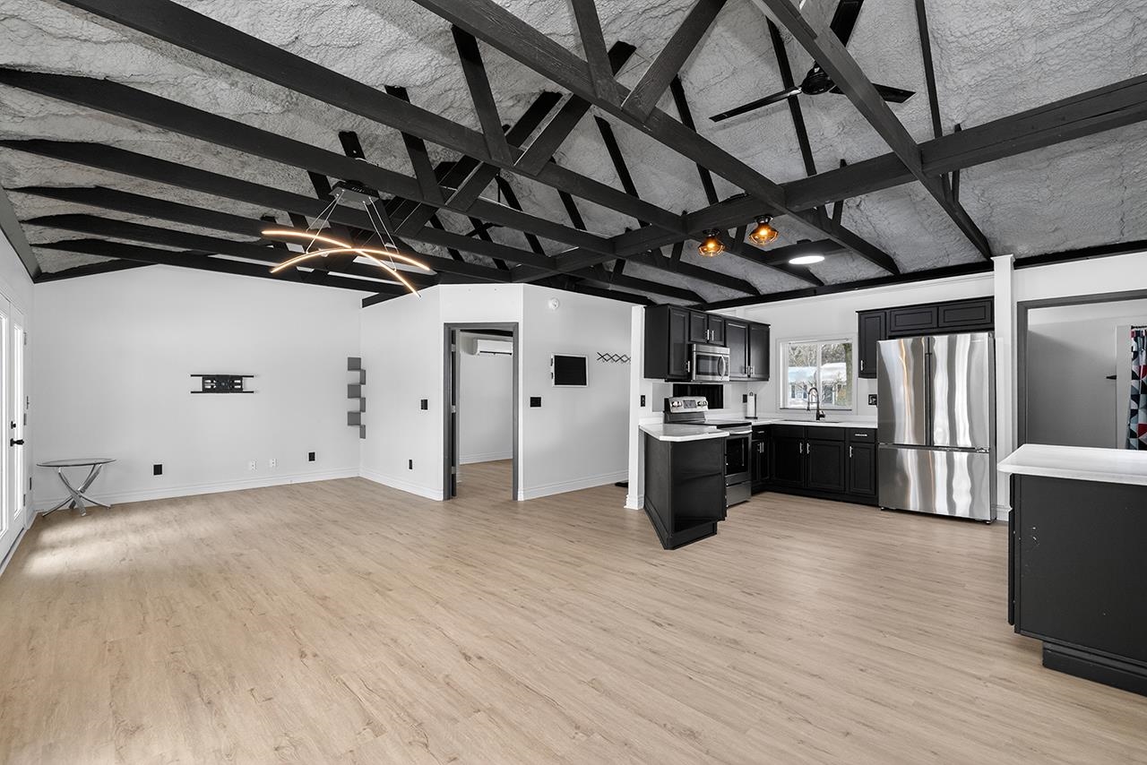 Kitchen featuring dark cabinetry, open floor plan, stainless steel appliances, light wood-type flooring, and beam ceiling