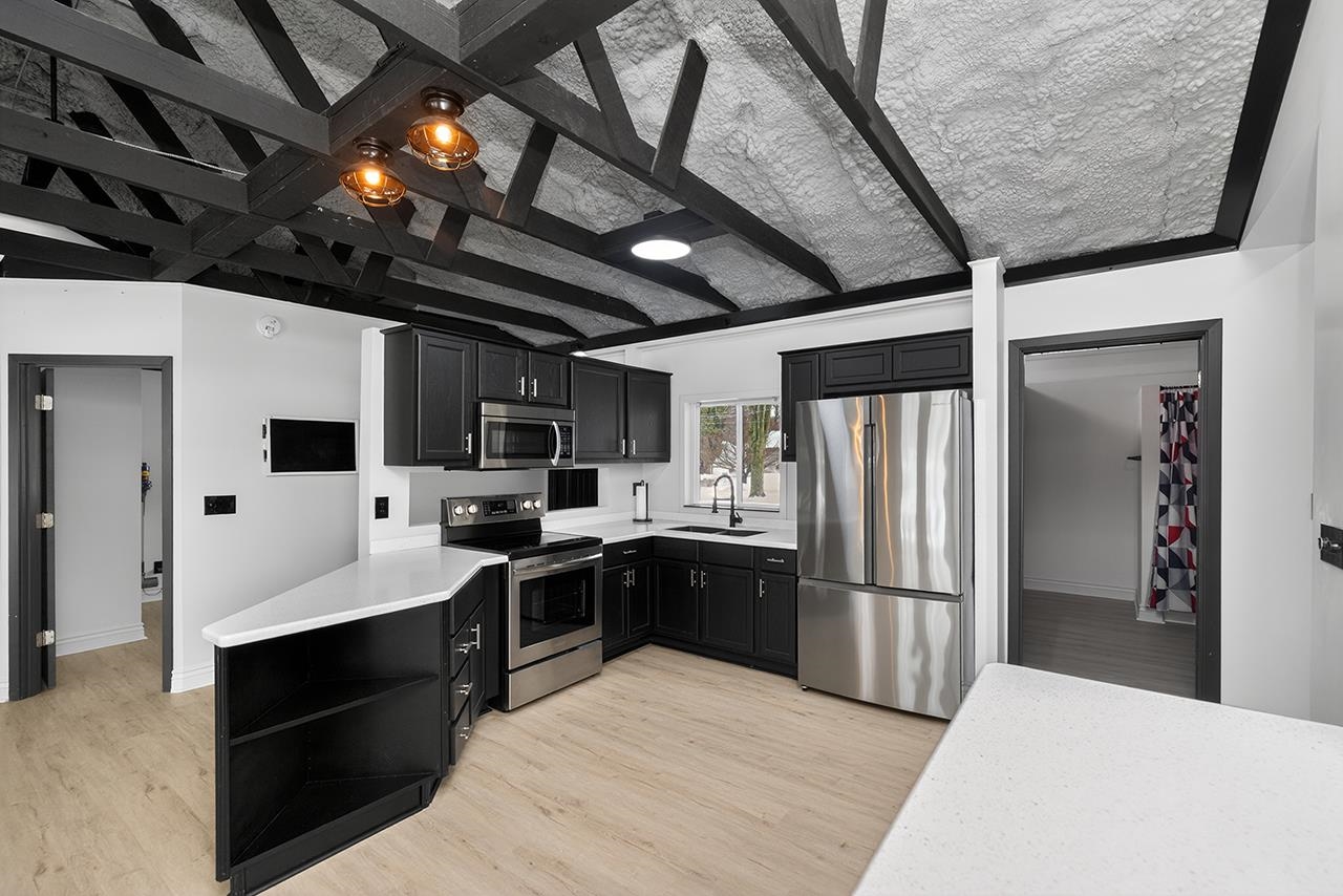 Kitchen featuring appliances with stainless steel finishes, dark cabinets, a peninsula, light wood-style floors, and open shelves