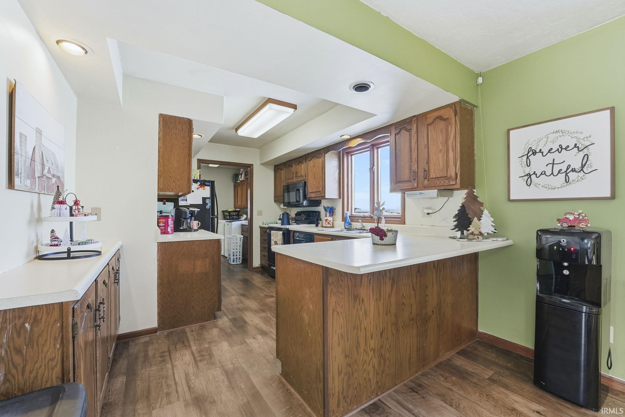 Kitchen with light countertops, brown cabinetry, a peninsula, dark wood-type flooring, and black appliances