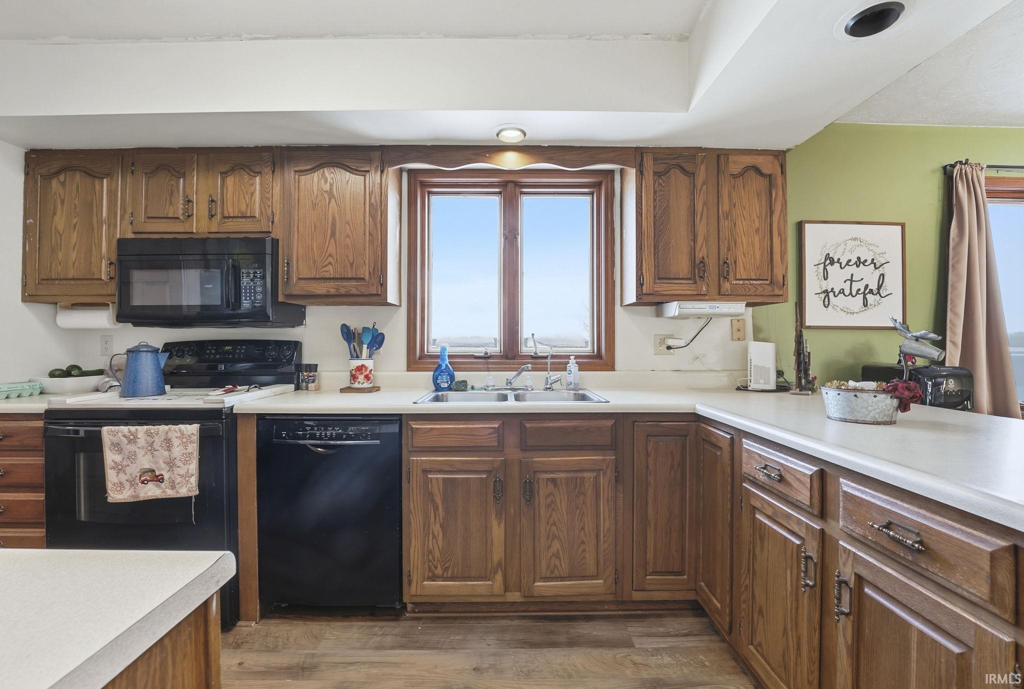 Kitchen featuring black appliances, light countertops, wood finished floors, and brown cabinetry