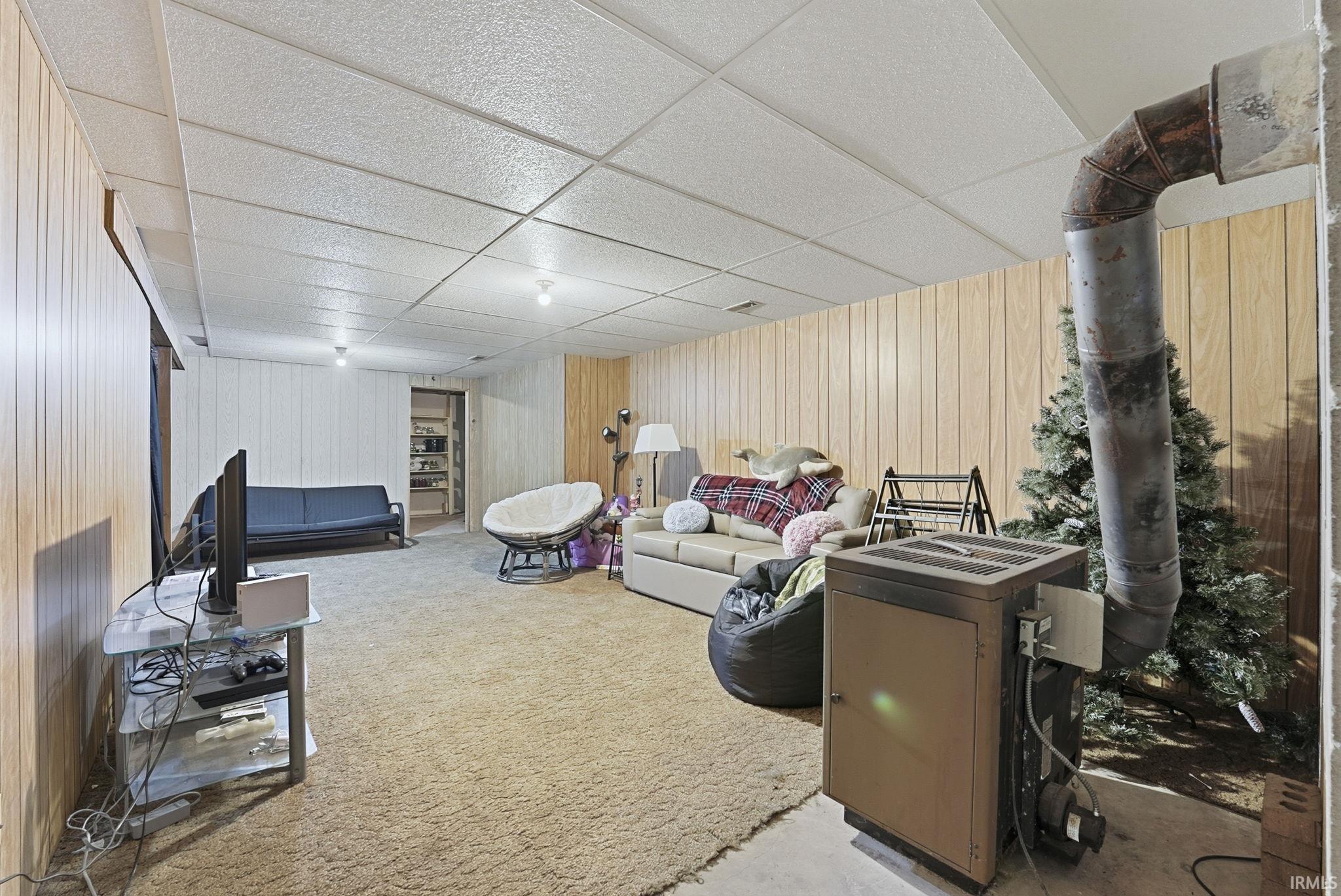Living room with a paneled ceiling, wood walls, and light colored carpet