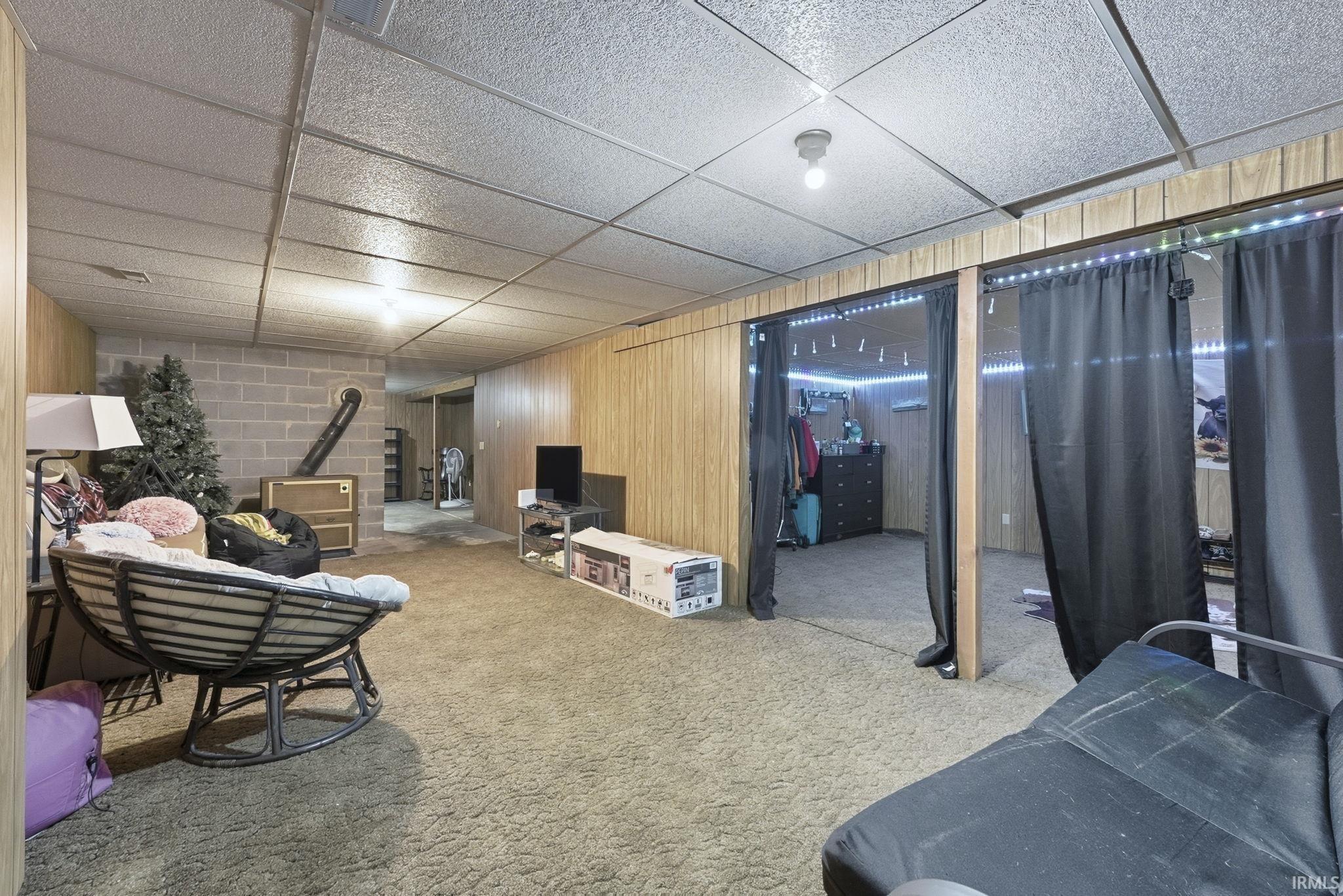 Finished basement with a paneled ceiling, wood walls, and carpet floors