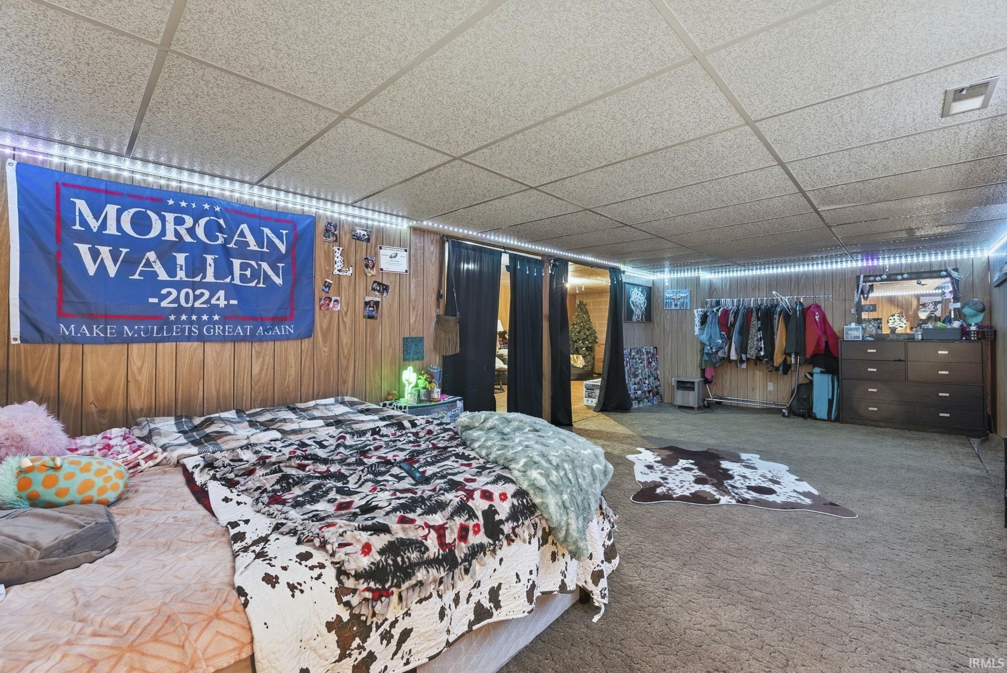 Bedroom with a drop ceiling, carpet flooring, and wood walls