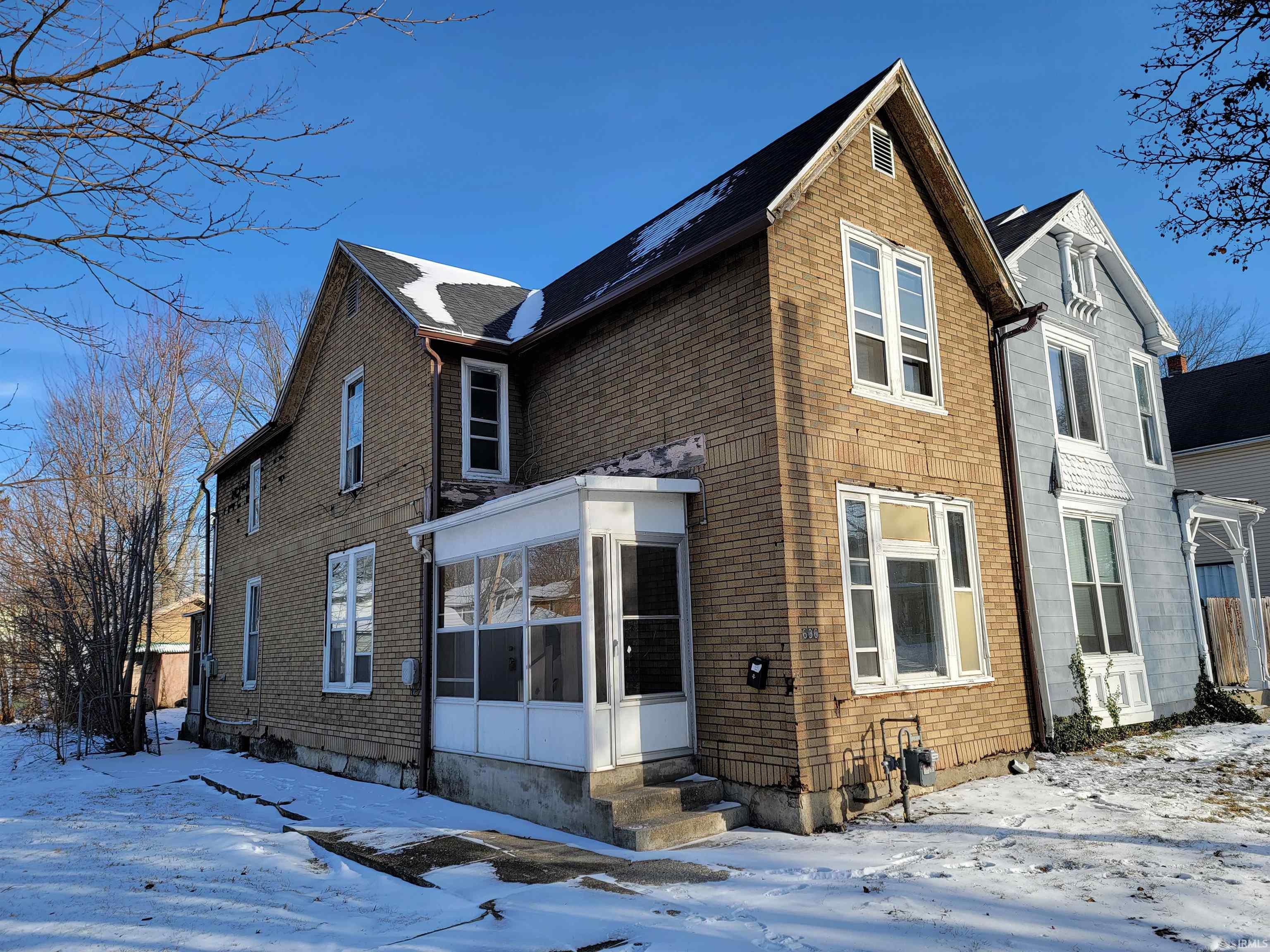 View of snowy exterior with a sunroom, brick siding, and entry steps