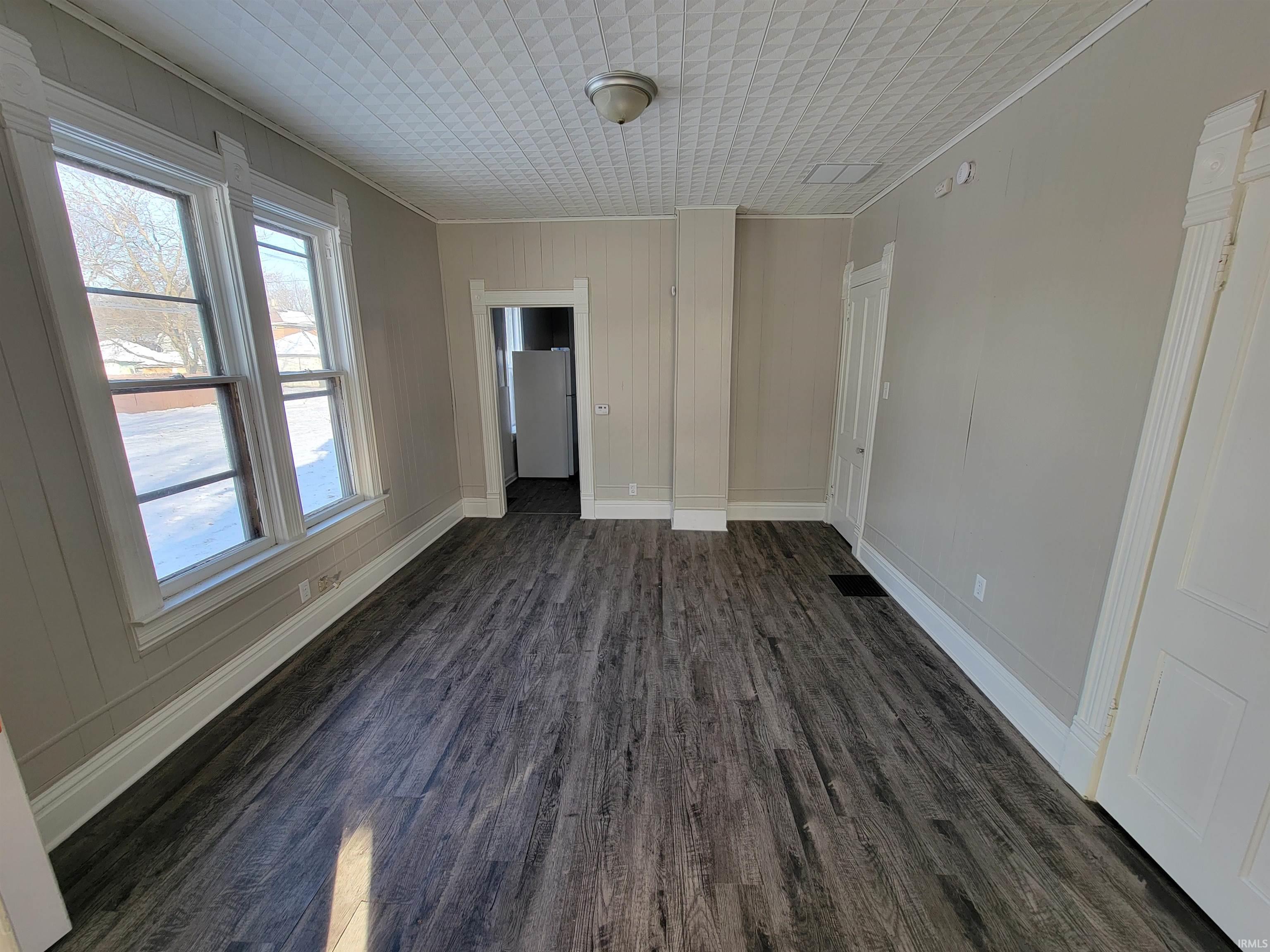Spare room featuring dark wood-style floors, ornamental molding, and wood walls