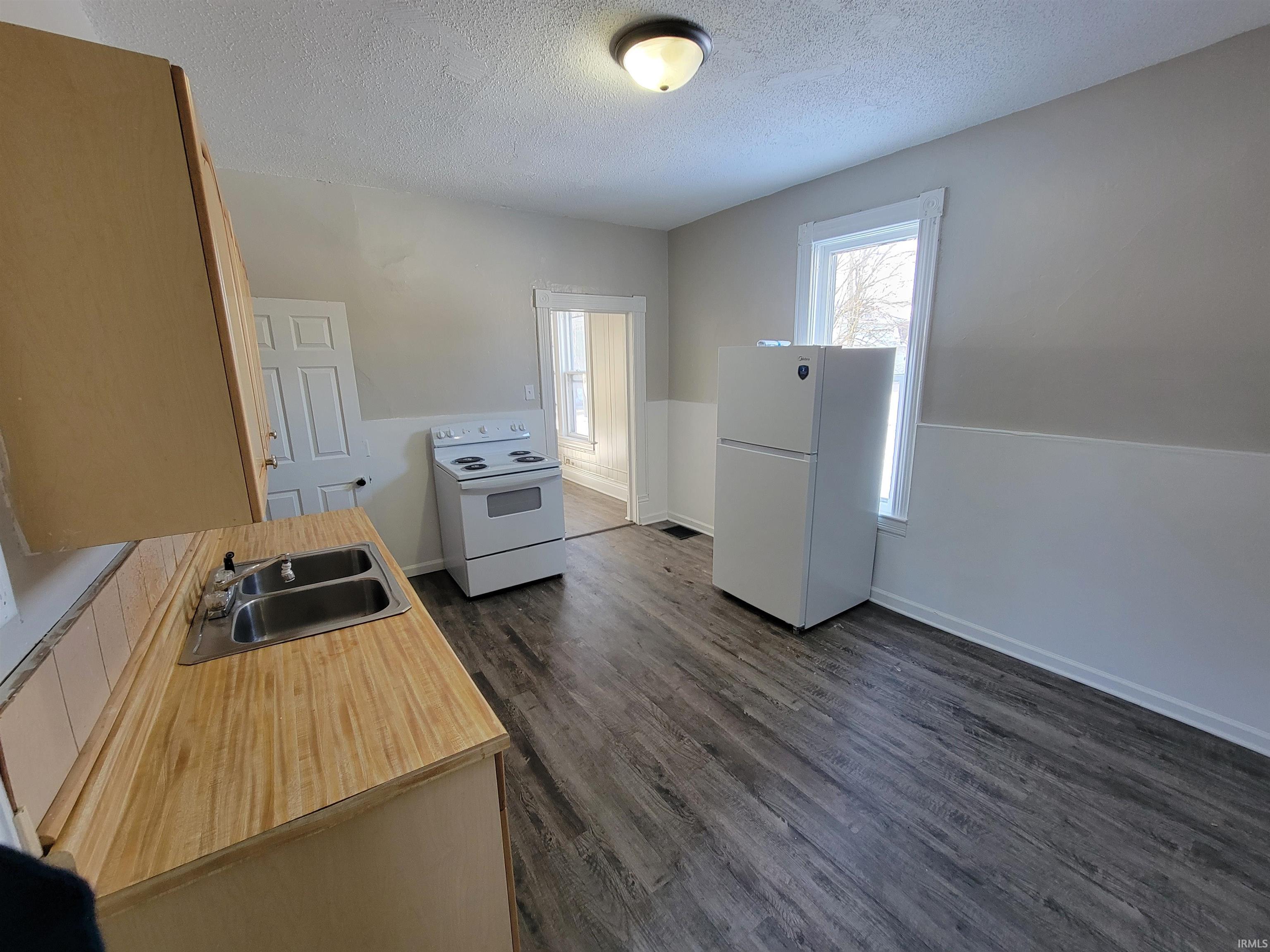 Kitchen with white appliances, light countertops, a textured ceiling, and dark wood-type flooring