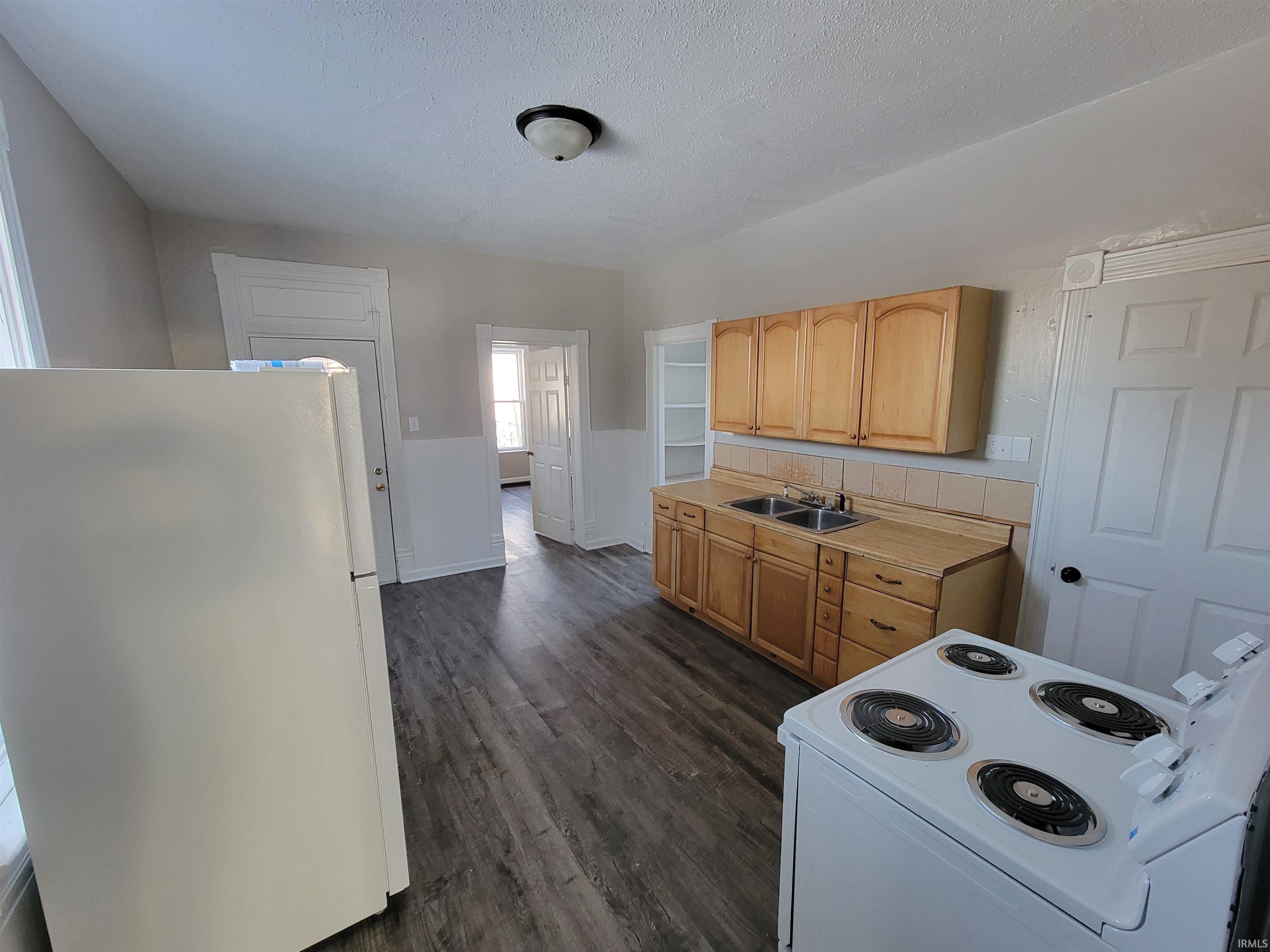 Kitchen with white appliances, light countertops, dark wood finished floors, a textured ceiling, and light brown cabinetry