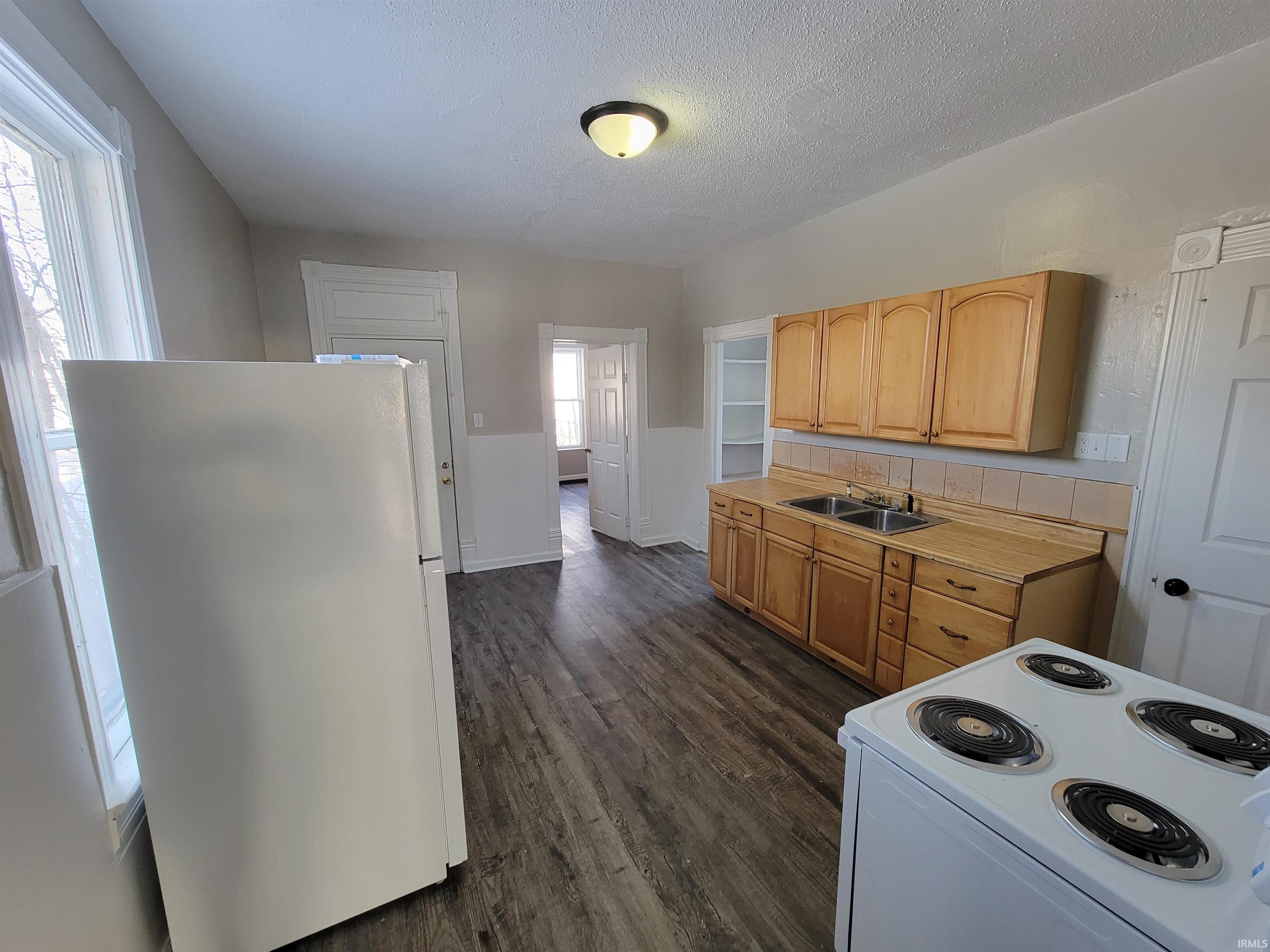 Kitchen featuring white appliances, light countertops, a textured ceiling, dark wood-style floors, and light brown cabinets