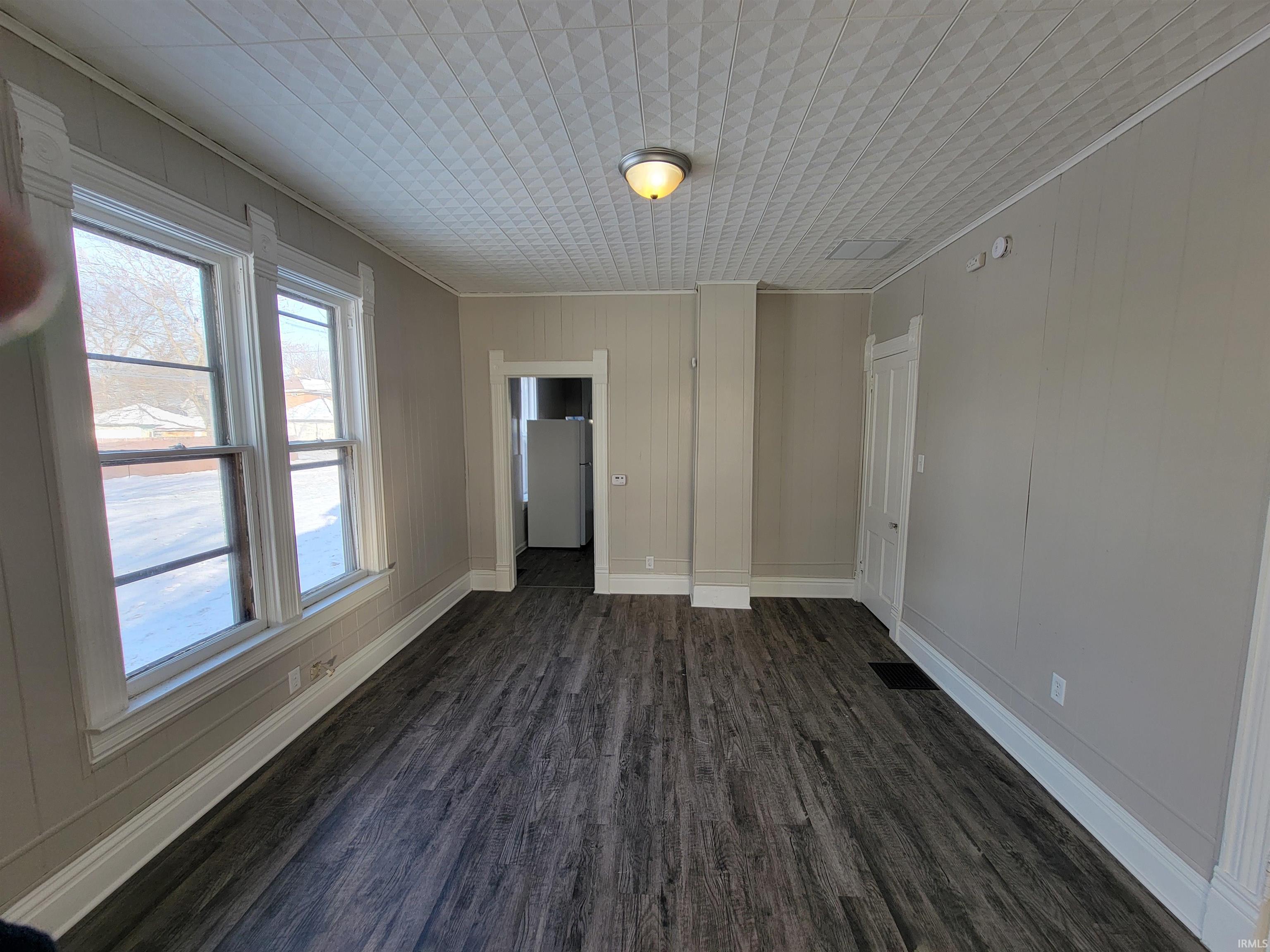 Unfurnished room featuring wooden walls, dark wood-type flooring, and crown molding