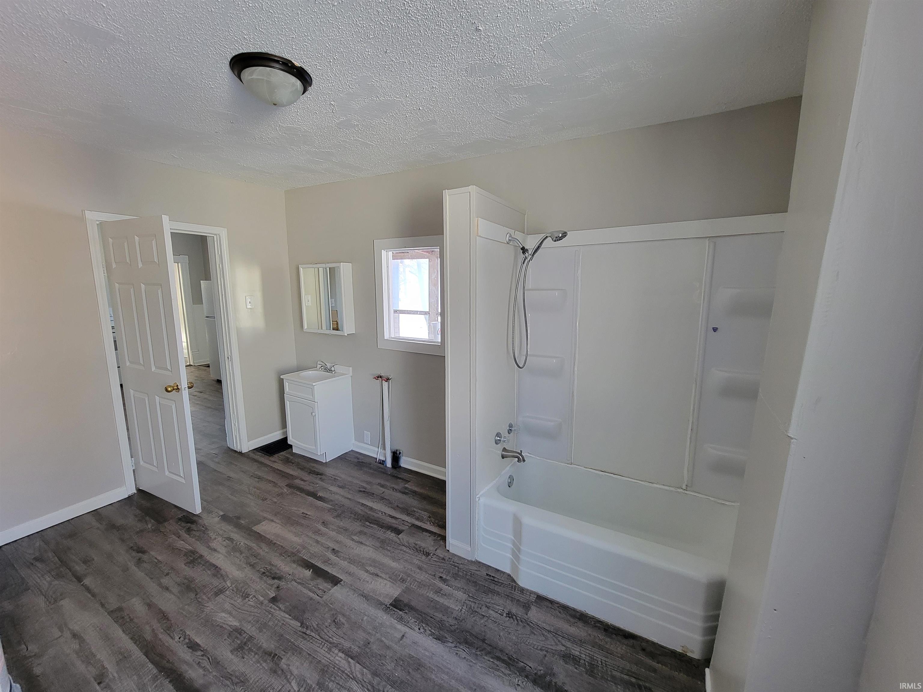 Bathroom with vanity, a textured ceiling, shower / bathtub combination, and dark wood-style floors