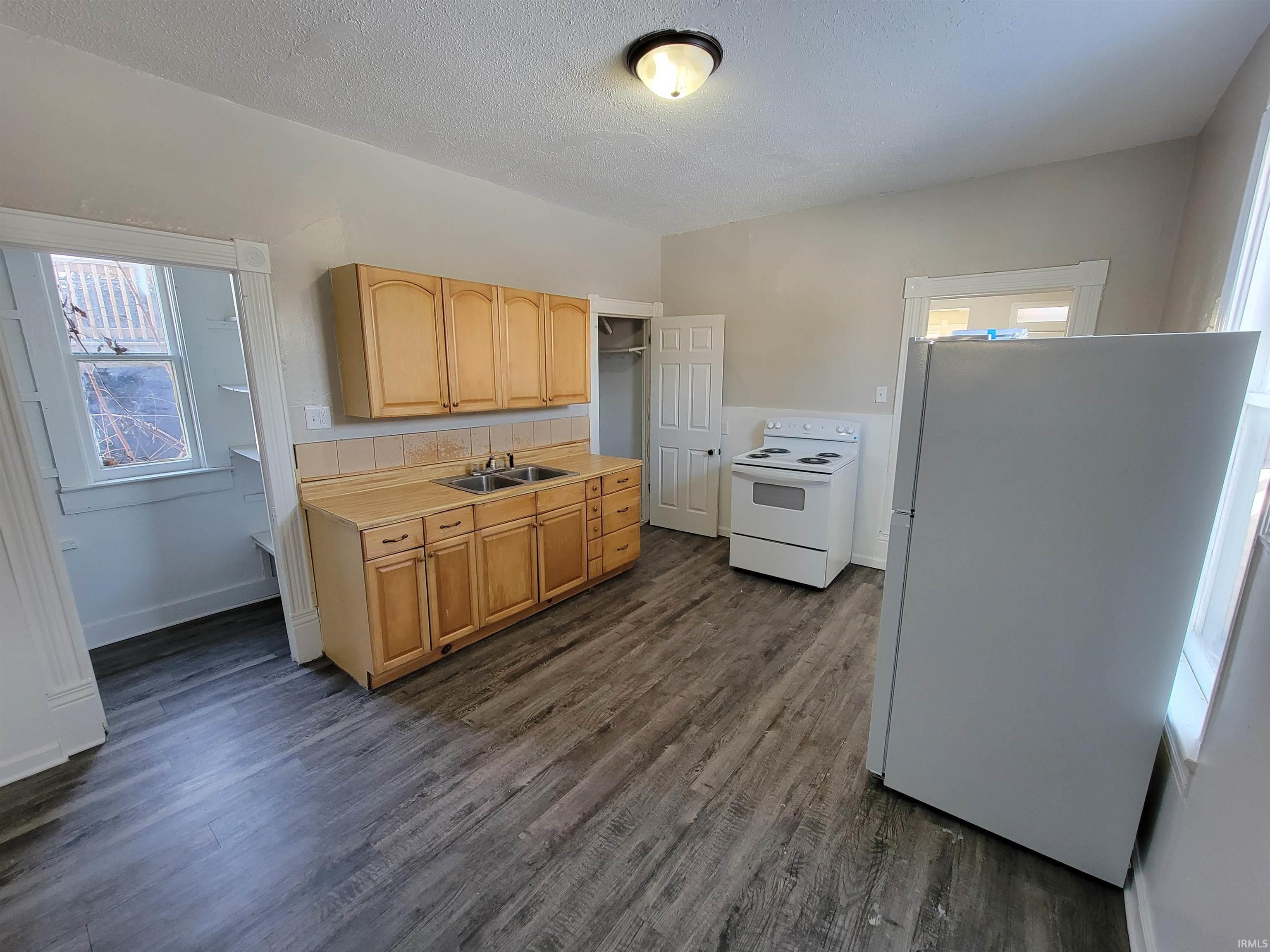 Kitchen featuring white appliances, light countertops, a textured ceiling, light brown cabinets, and dark wood-style floors
