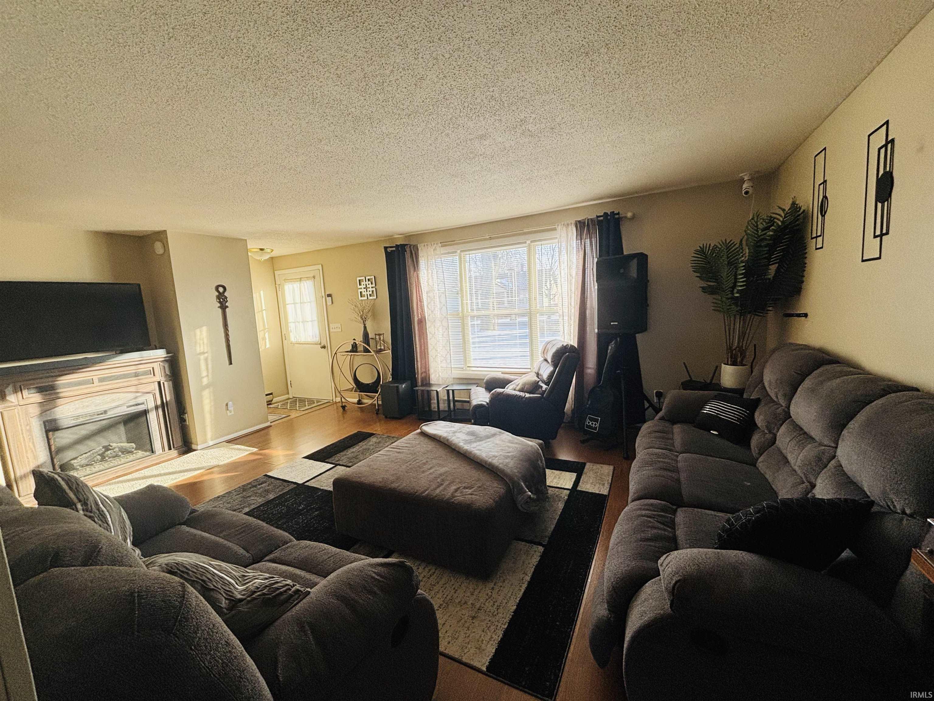 Living room with a textured ceiling, a fireplace with raised hearth, and wood finished floors
