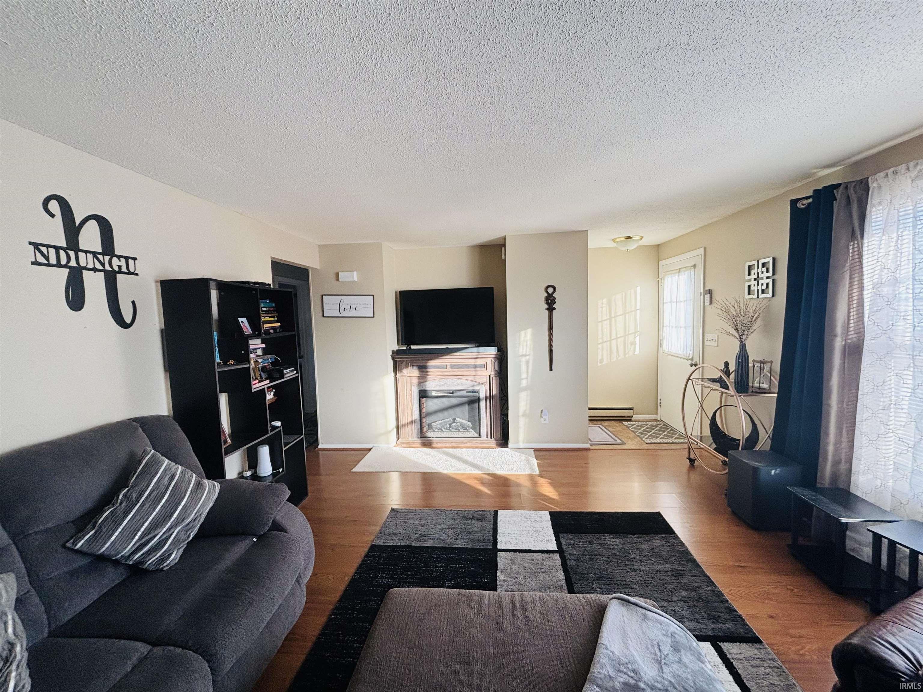 Living area featuring wood finished floors, a textured ceiling, a fireplace, and a baseboard heating unit