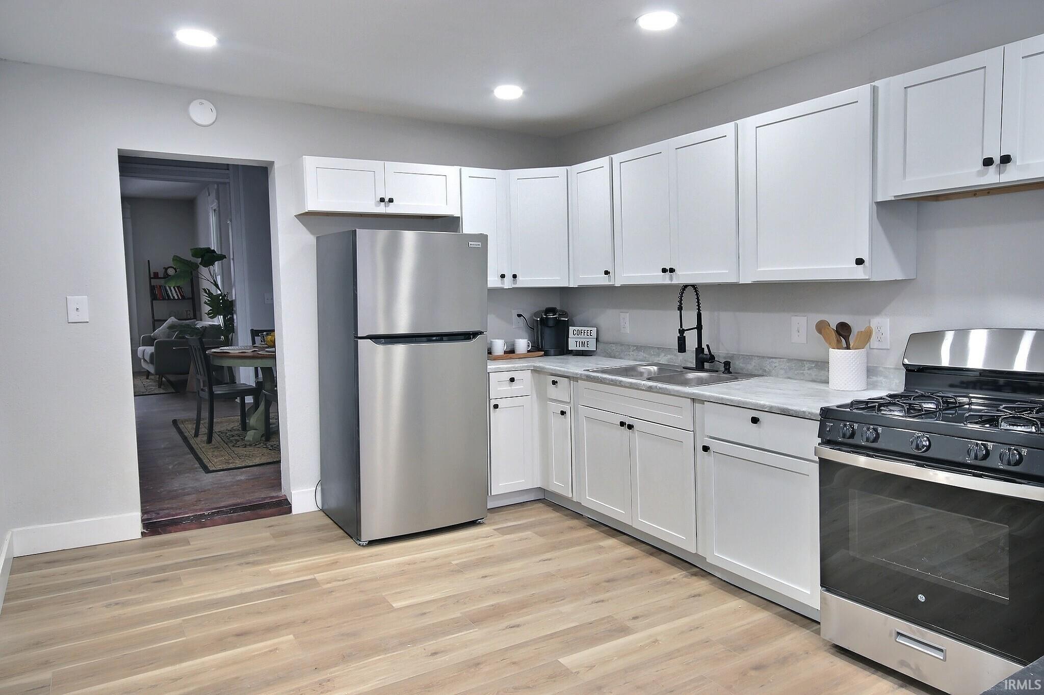 Kitchen with stainless steel appliances, white cabinets, light wood-style flooring, and recessed lighting