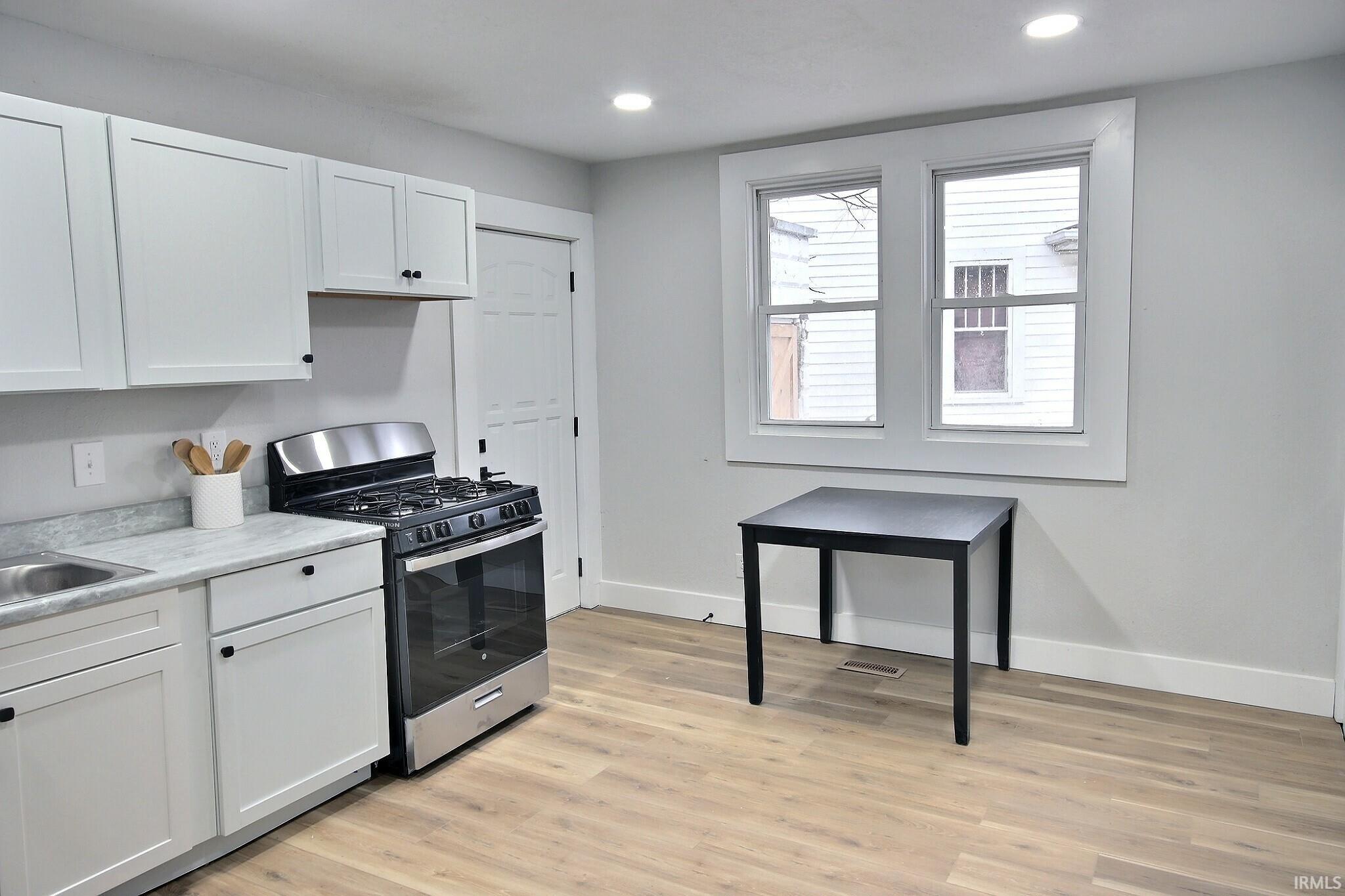 Kitchen featuring gas range, light countertops, white cabinets, light wood-style floors, and recessed lighting