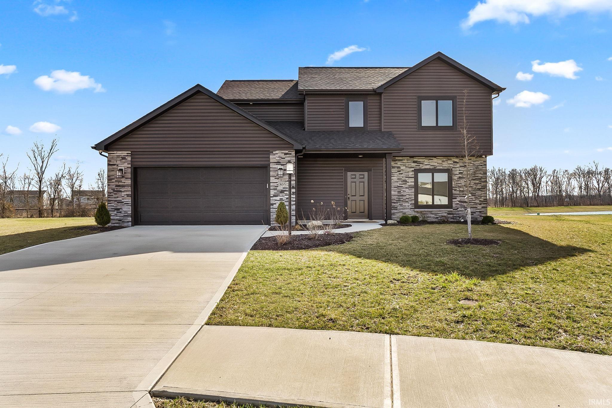 Traditional-style home with stone siding, a front lawn, driveway, roof with shingles, and a garage