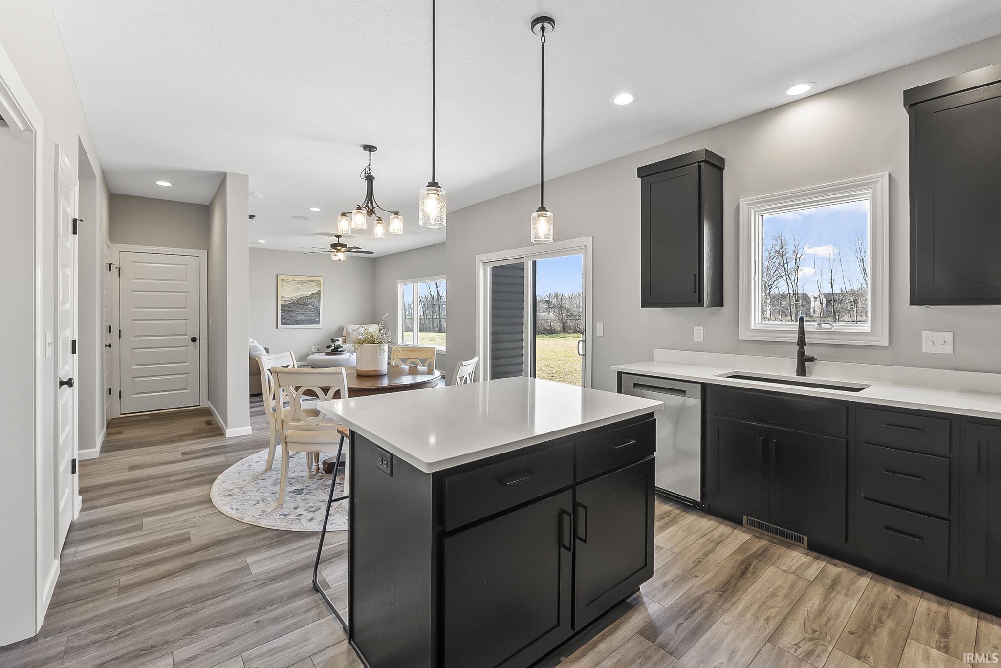 Kitchen with dark cabinets, open floor plan, a kitchen island, dishwasher, and light wood-type flooring