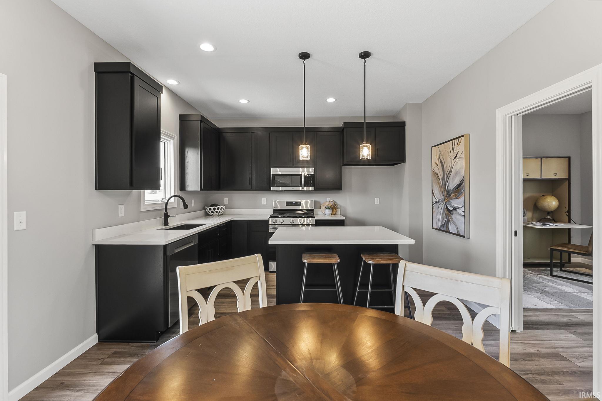 Kitchen featuring dark cabinetry, stainless steel appliances, a center island, light wood finished floors, and decorative light fixtures