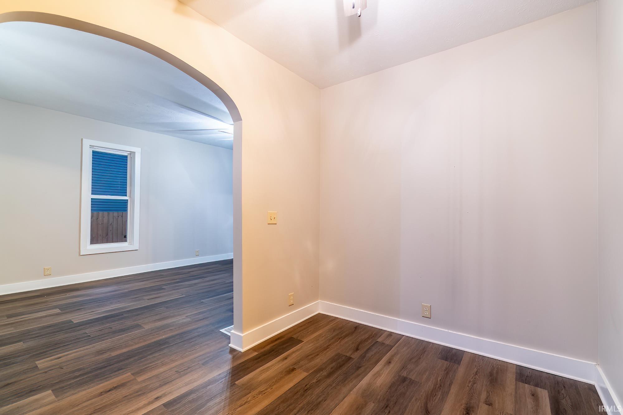 Unfurnished room featuring arched walkways and dark wood-style floors