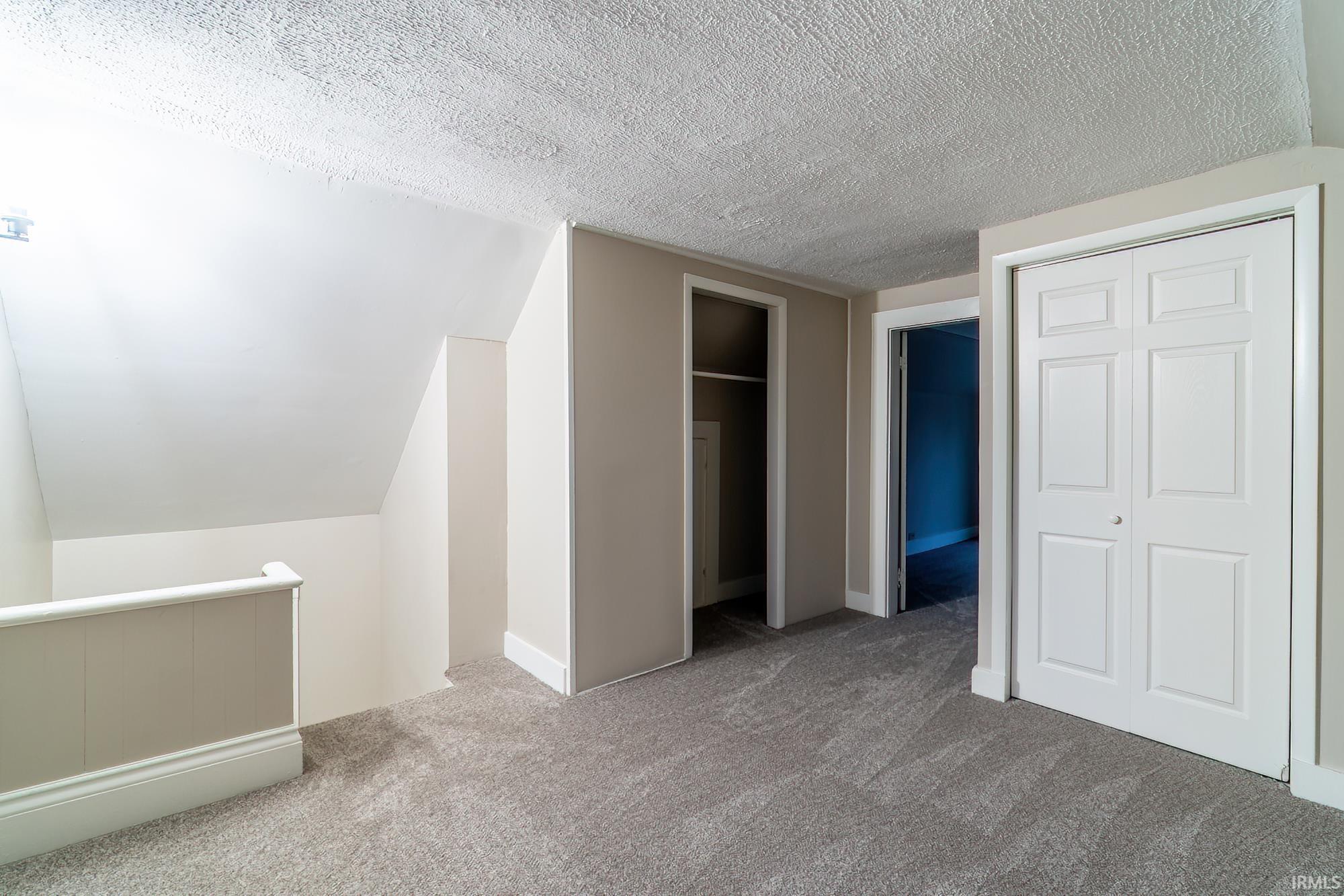 Unfurnished bedroom with vaulted ceiling, carpet, a textured ceiling, and multiple closets