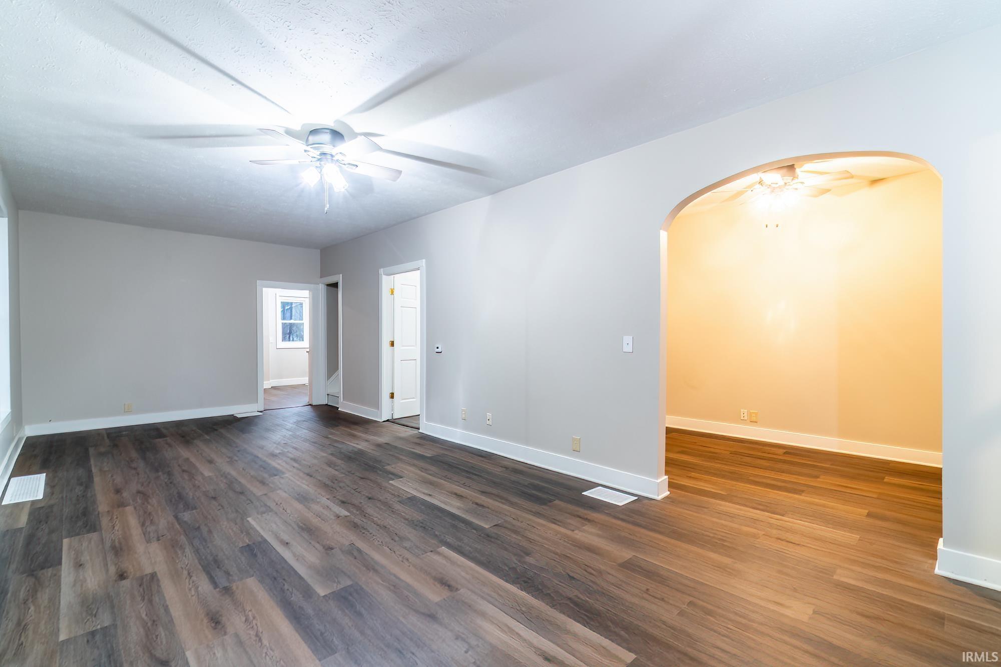 Unfurnished room featuring ceiling fan, dark wood-type flooring, and arched walkways