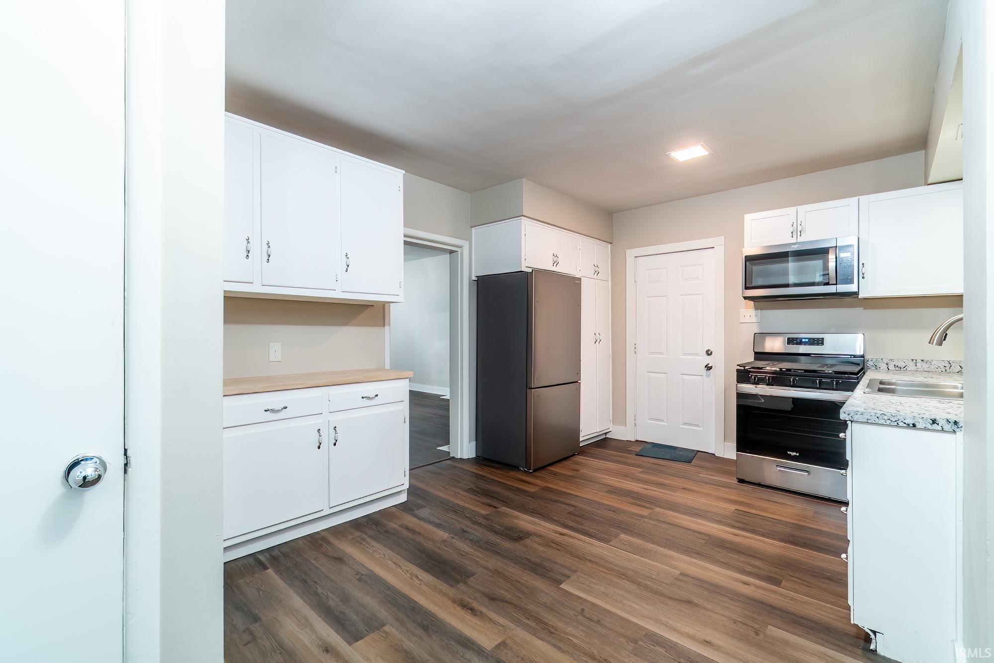 Kitchen with stainless steel appliances, light countertops, white cabinetry, and dark wood-style flooring