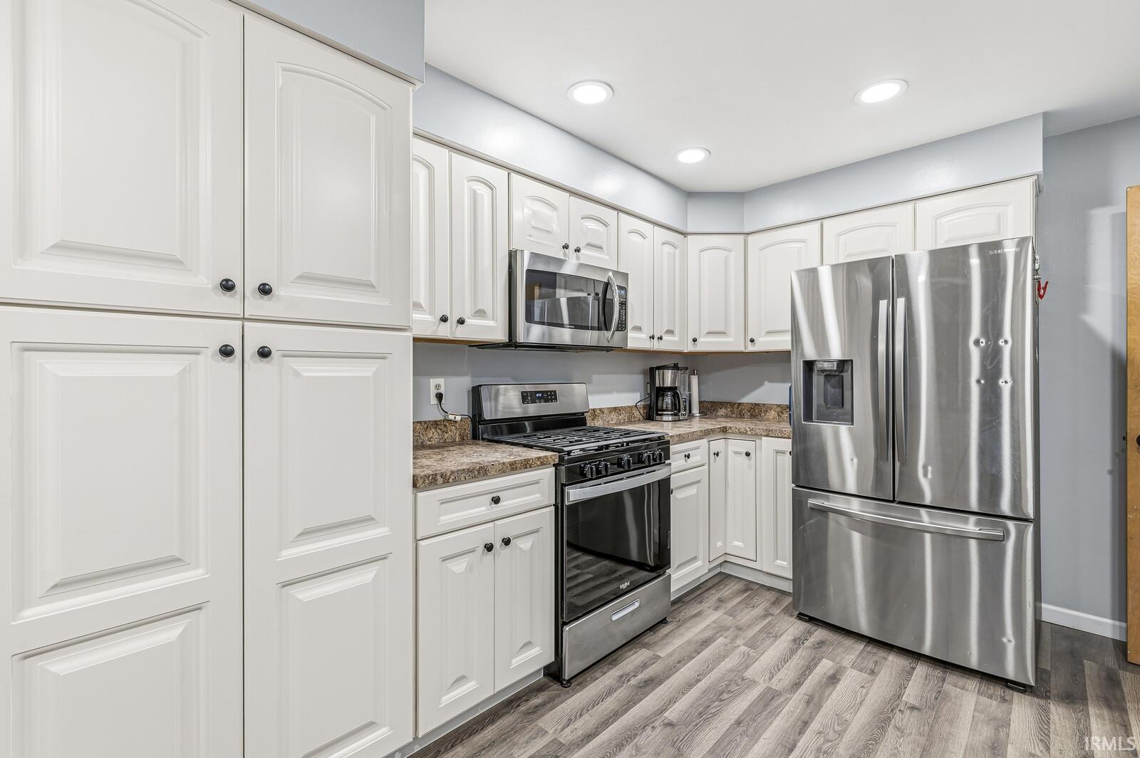 Kitchen with stainless steel appliances, white cabinetry, light wood-type flooring, recessed lighting, and dark countertops