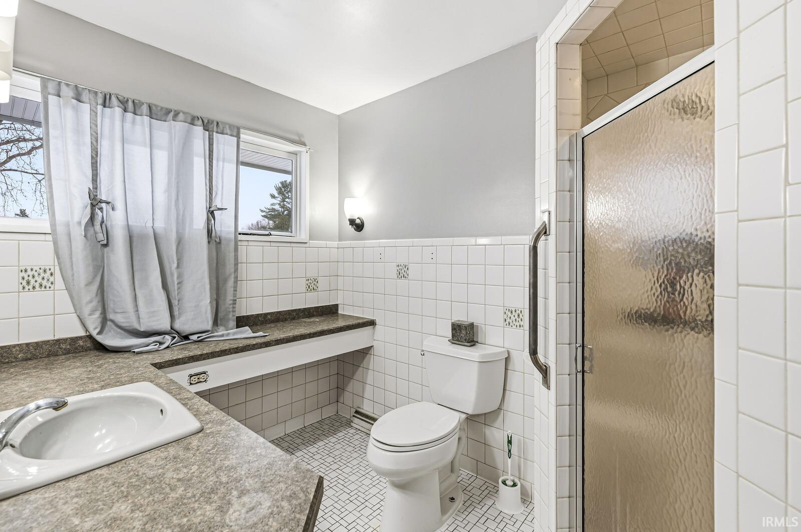 Full bathroom featuring vanity, tile walls, wainscoting, light tile patterned flooring, and a shower stall