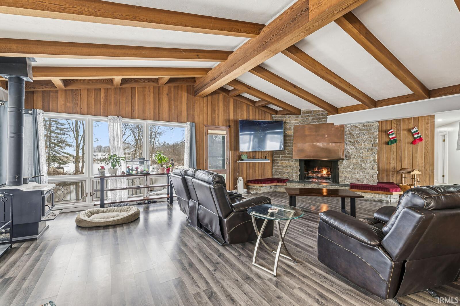 Living room featuring wooden walls, a wood stove, a large fireplace, and wood finished floors