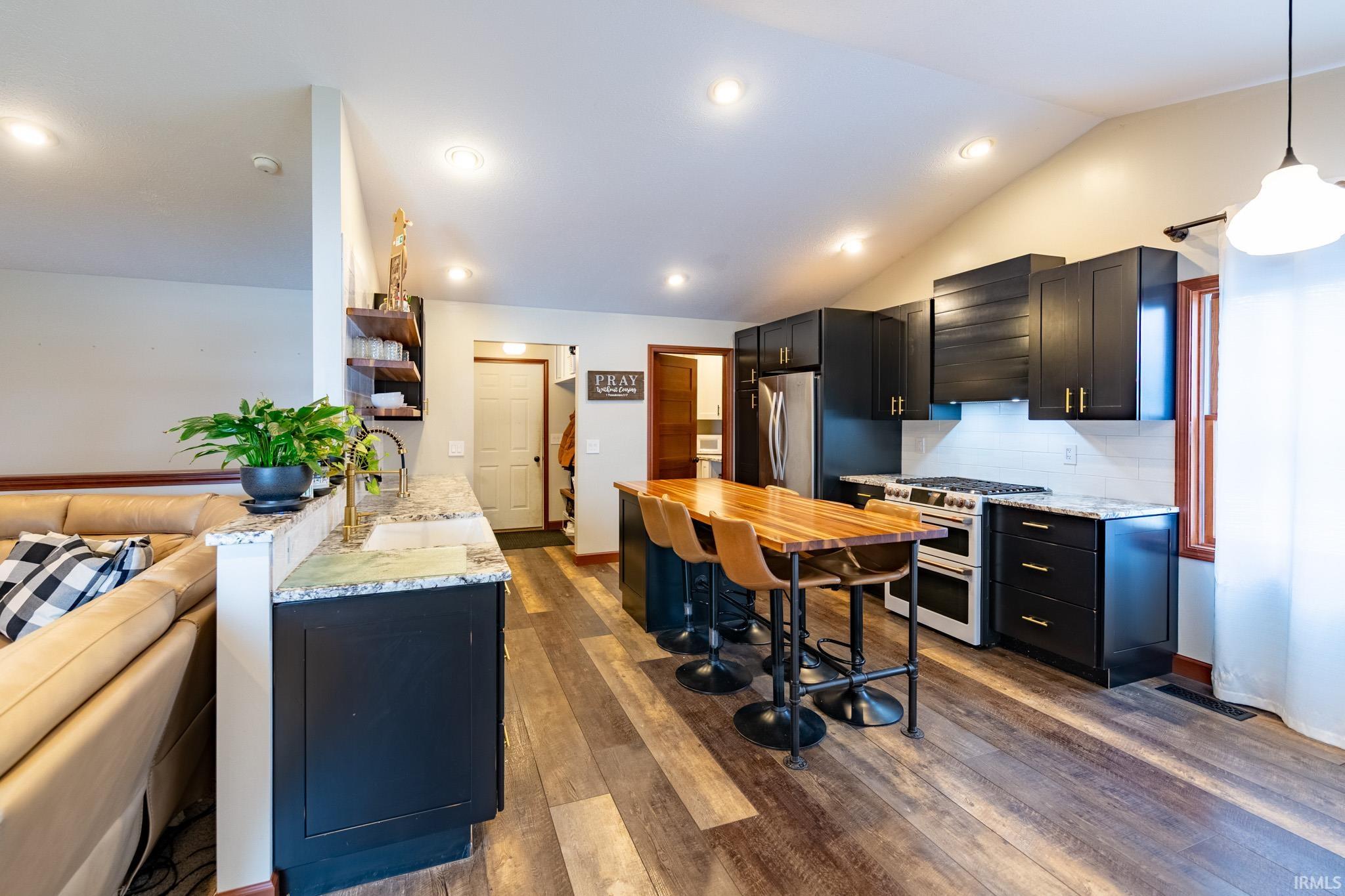 Kitchen featuring dark cabinets, light stone countertops, range with two ovens, lofted ceiling, and dark wood finished floors