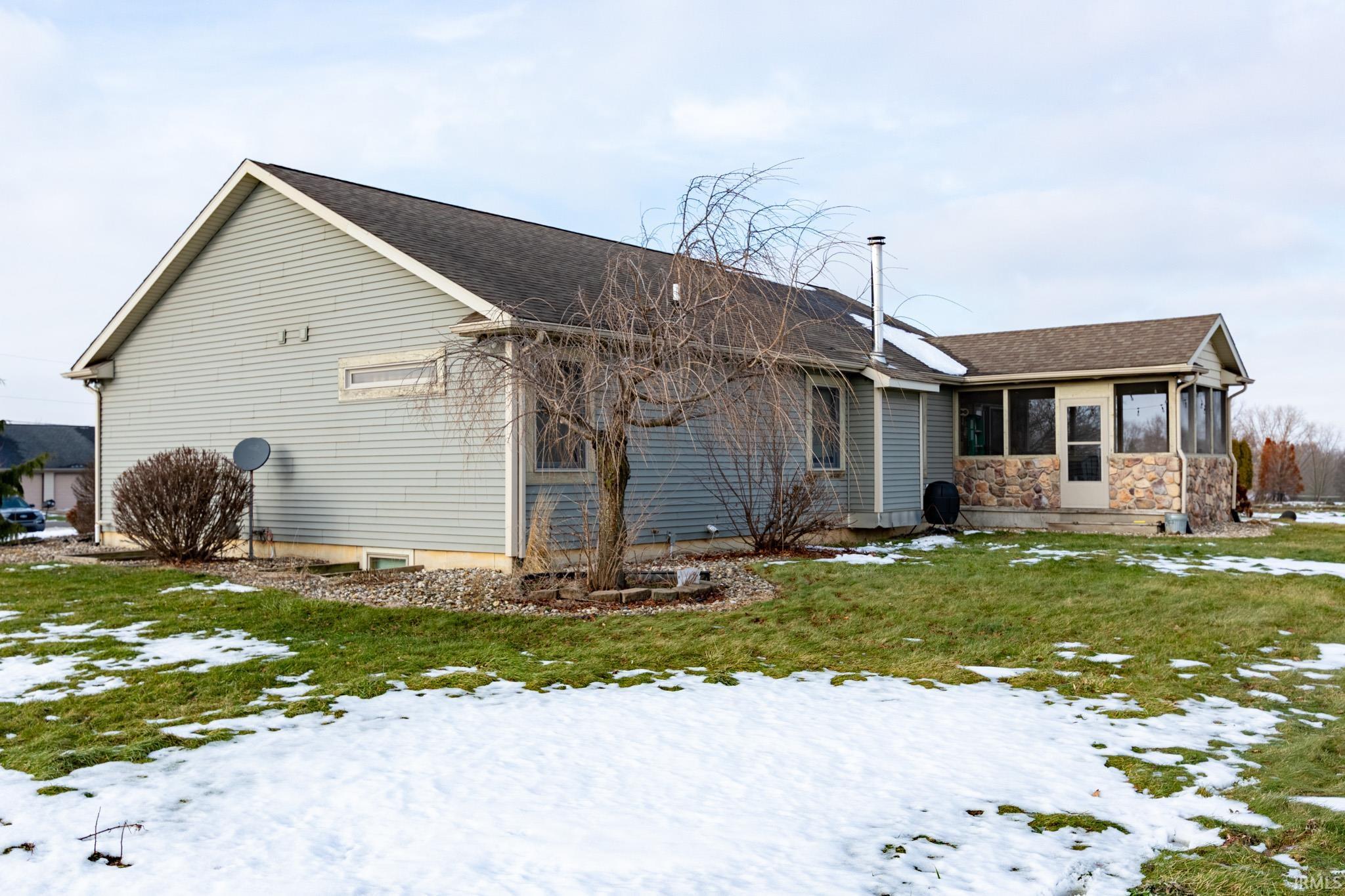 Snow covered property with a sunroom, a yard, roof with shingles, and stone siding