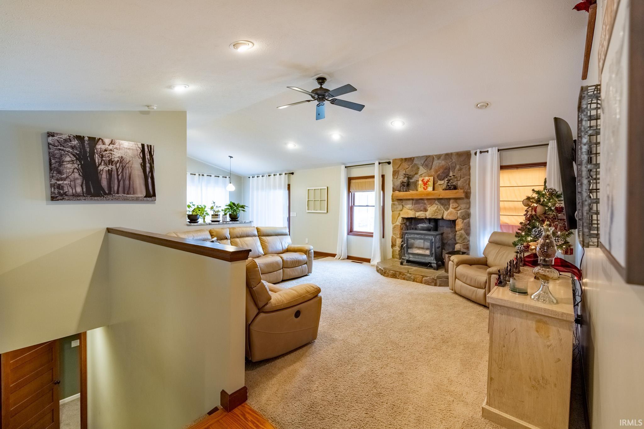 Living area with lofted ceiling, a ceiling fan, healthy amount of natural light, light colored carpet, and a wood stove