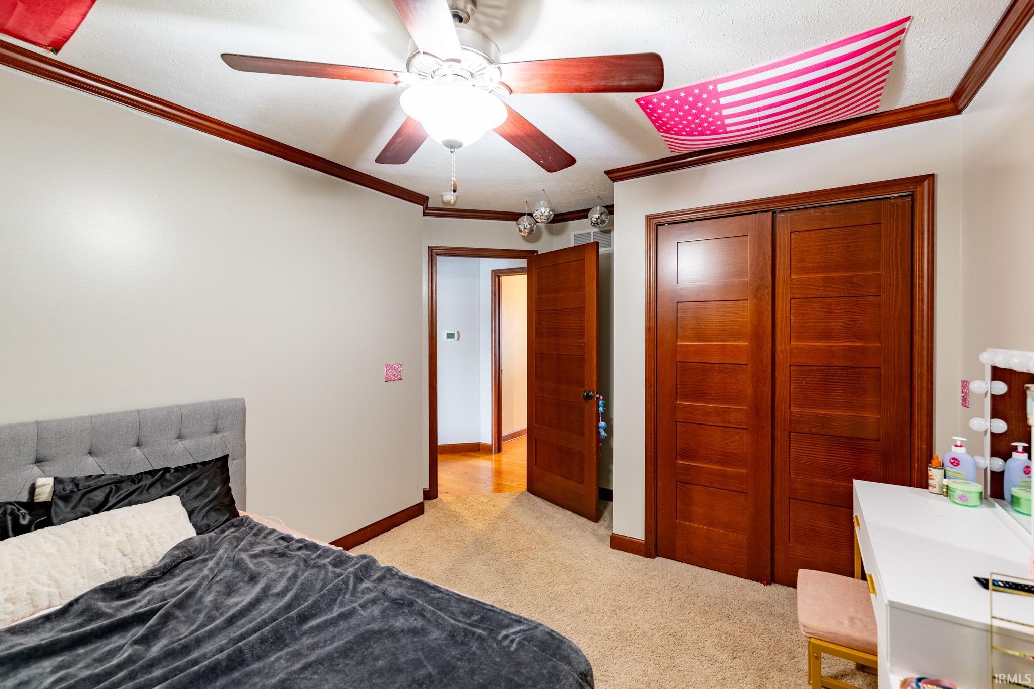 Bedroom with ornamental molding, light carpet, a closet, and a ceiling fan