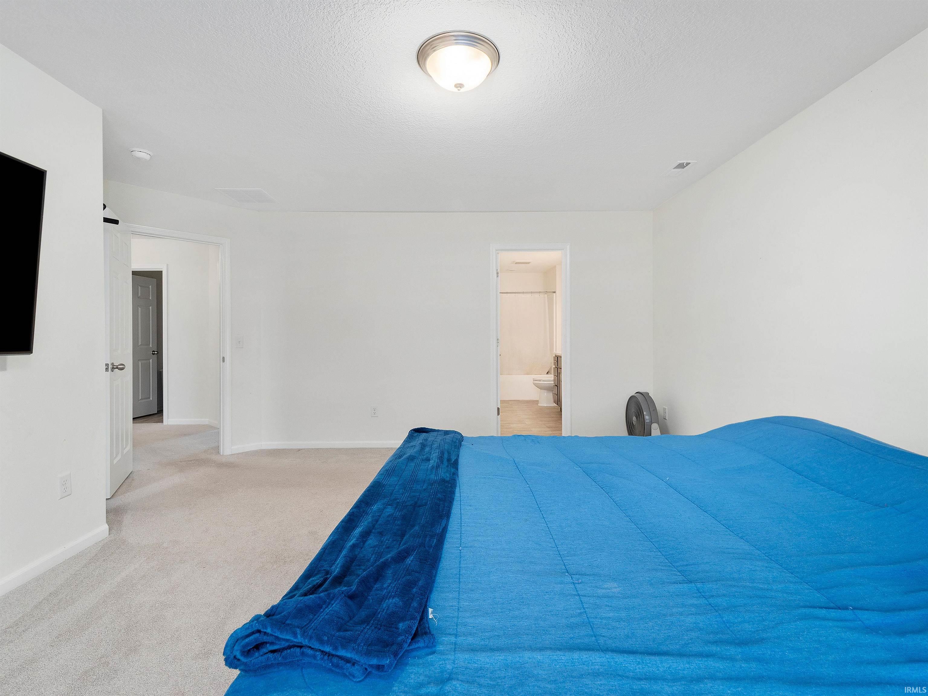 Bedroom with carpet, ensuite bath, and a textured ceiling