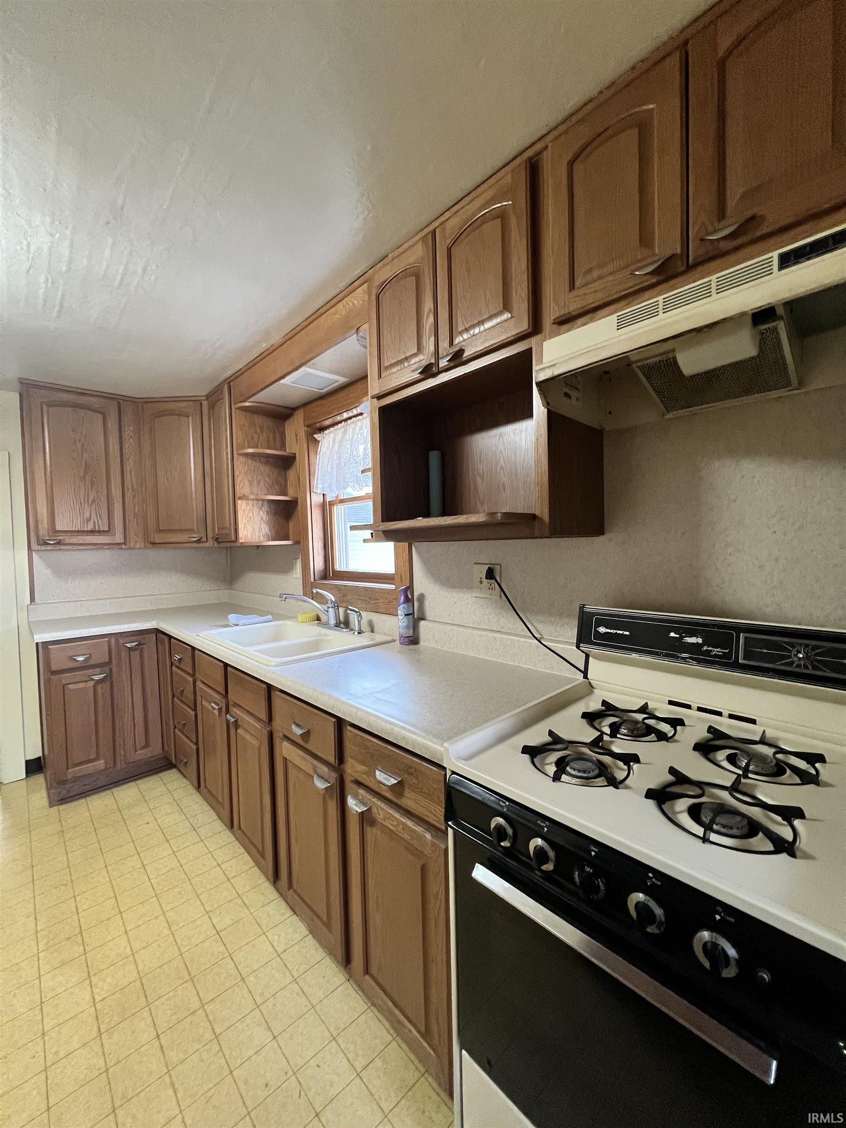 Kitchen with white gas range, under cabinet range hood, light countertops, and open shelves