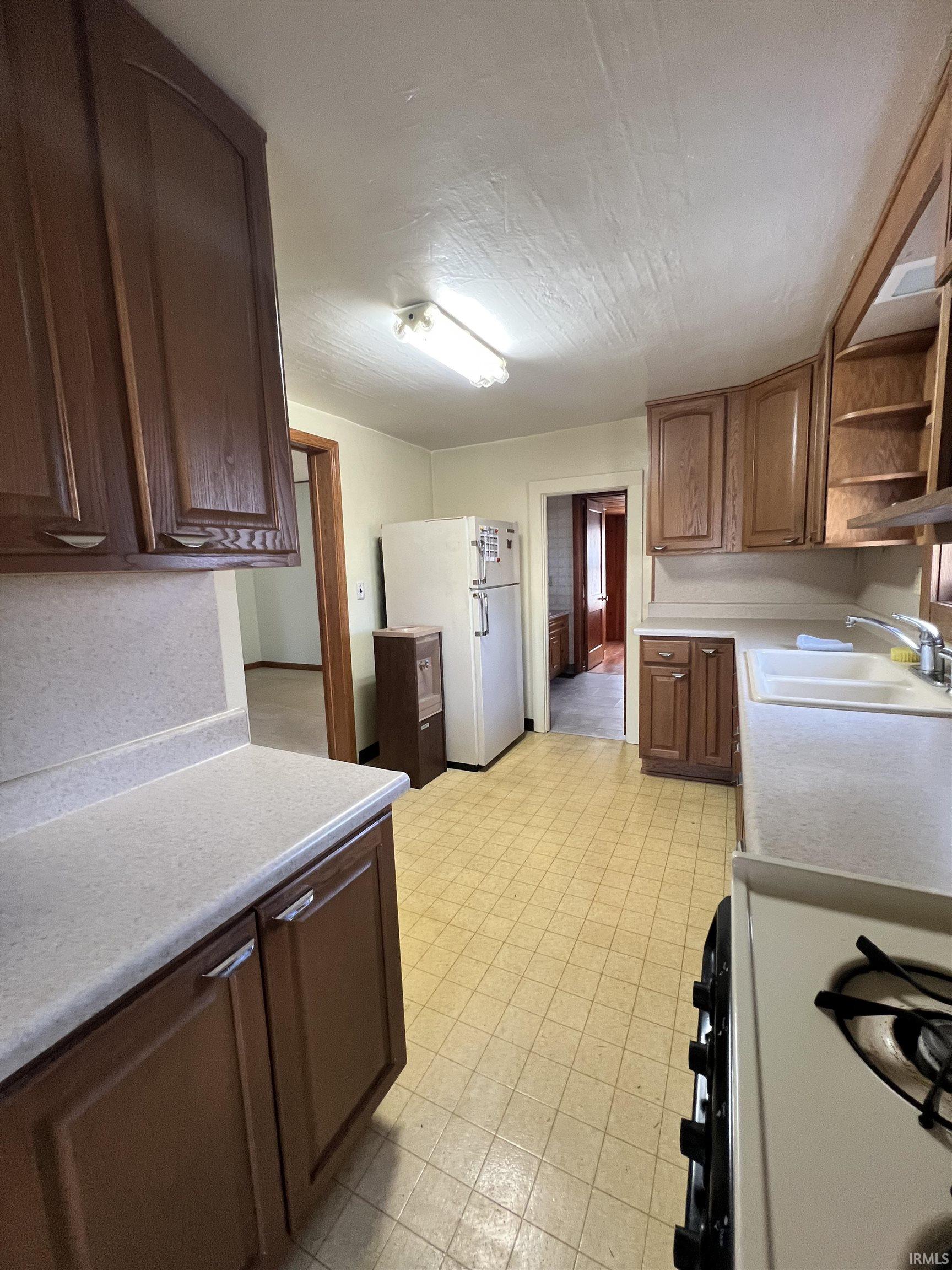 Kitchen with light countertops, open shelves, freestanding refrigerator, light floors, and gas stove