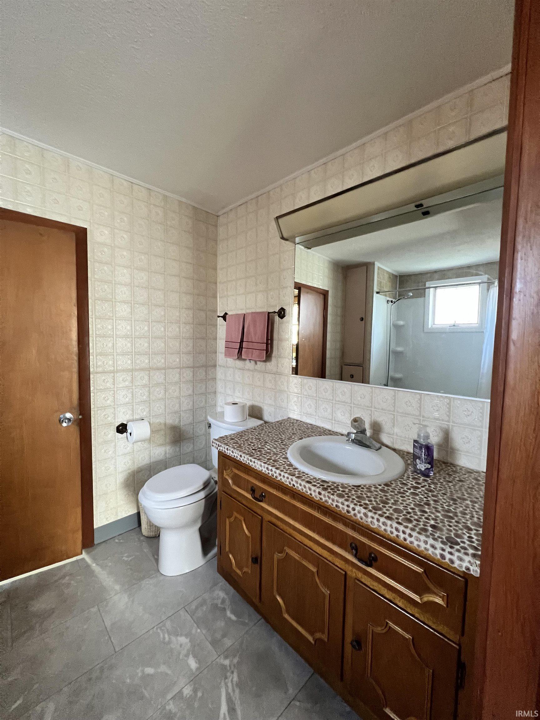 Full bath with vanity, a textured ceiling, a shower, and wallpapered walls